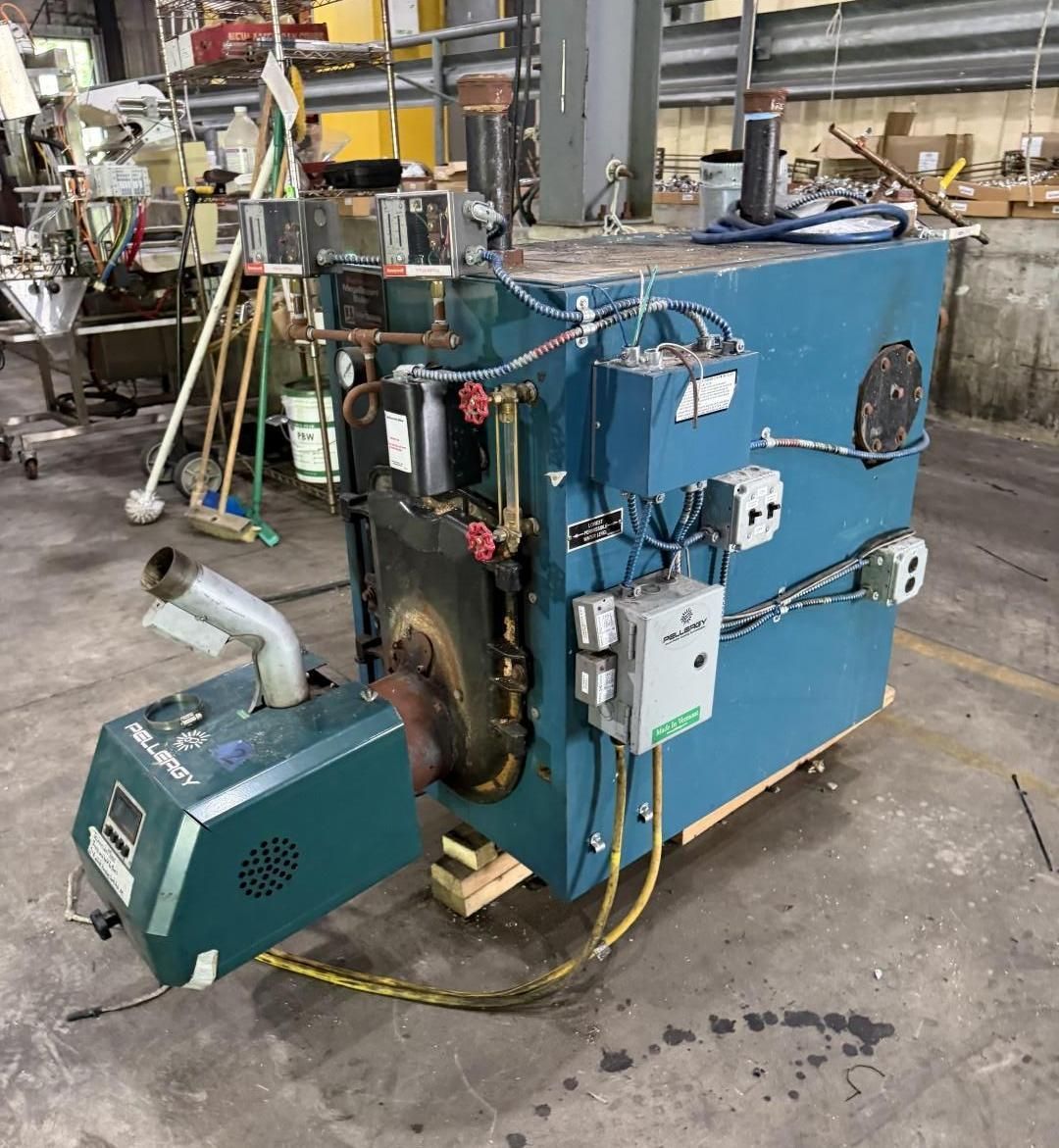 Blue industrial boiler in a warehouse, with attached pipes, gauges, and a green floor unit beside it.