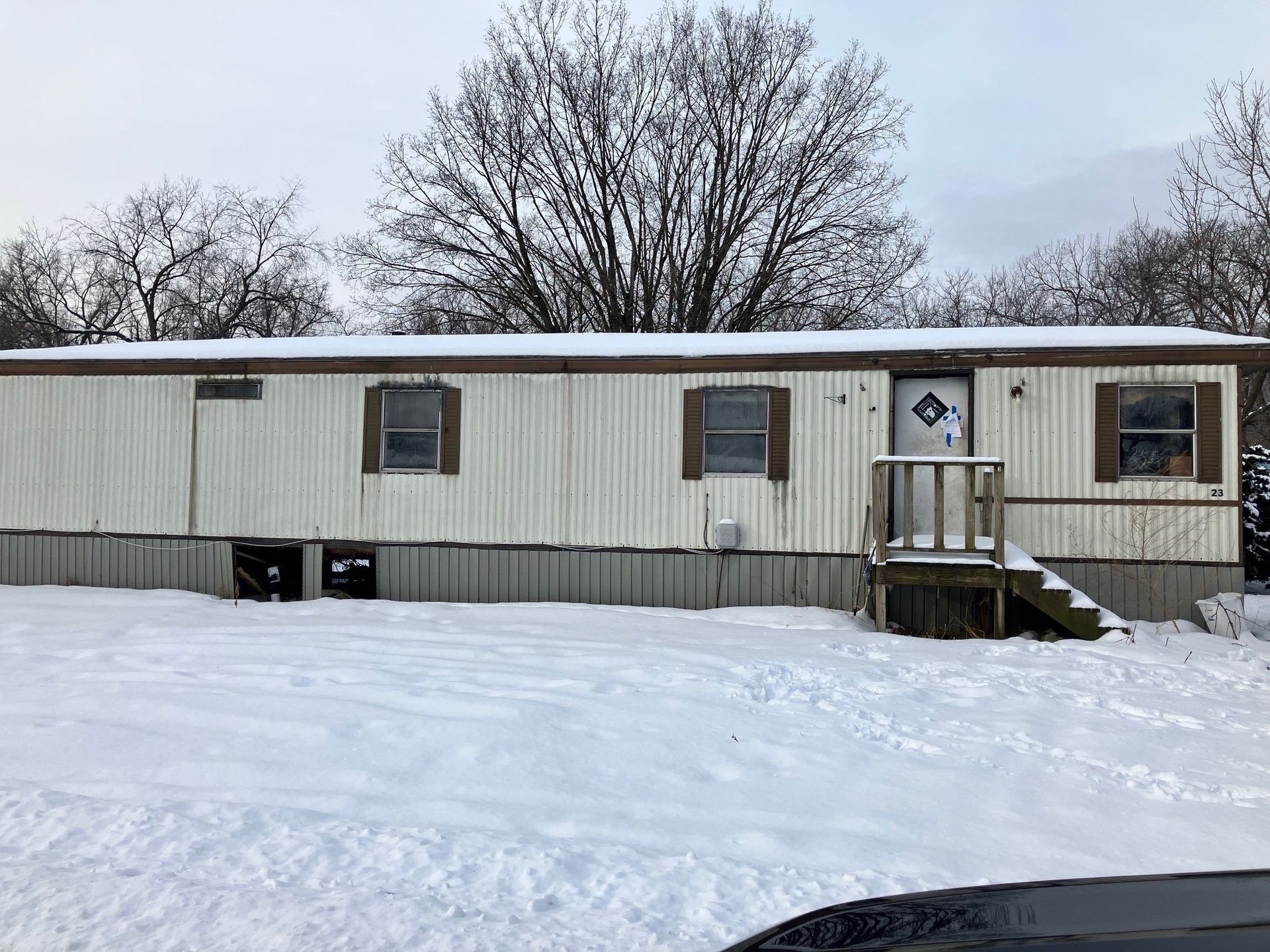 Mobile home in snowy setting; white siding, brown shutters, front porch with steps.