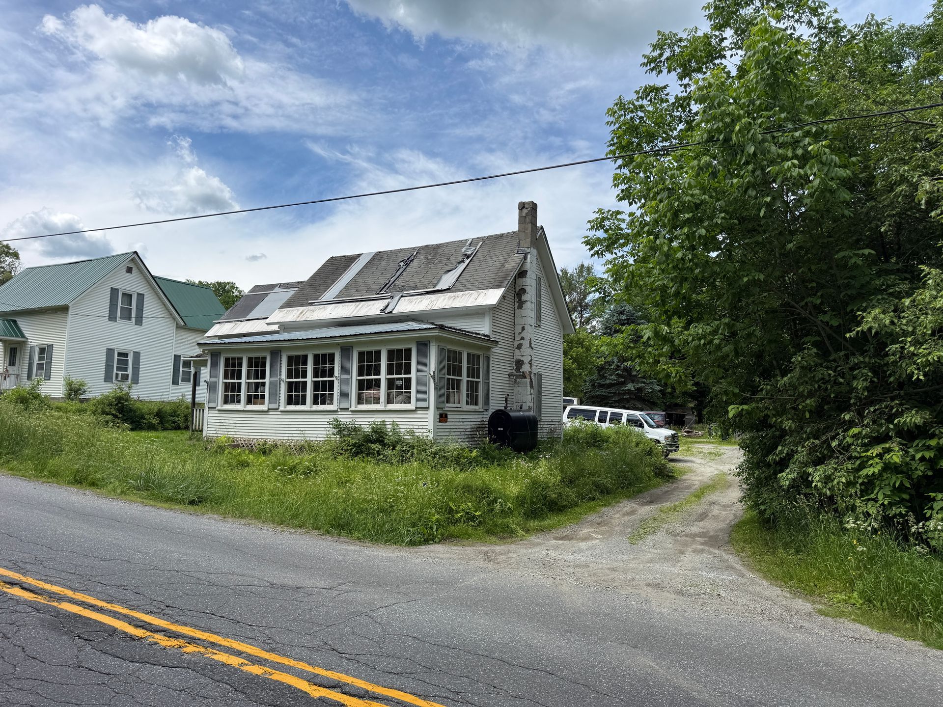 Small white house with a roof beside a road, under a partly cloudy sky