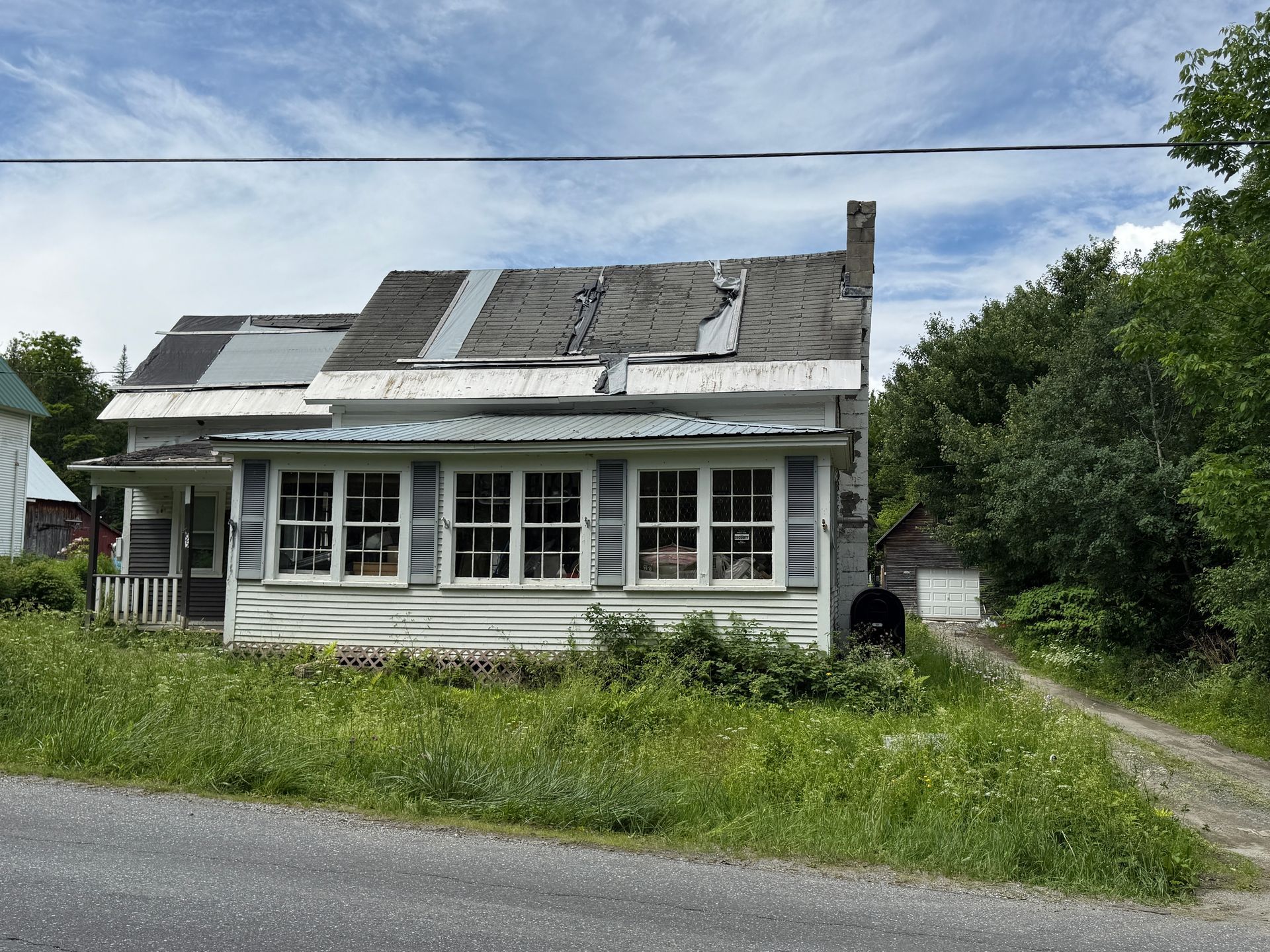 white house with roof beside a dirt road and grass under a cloudy sky
