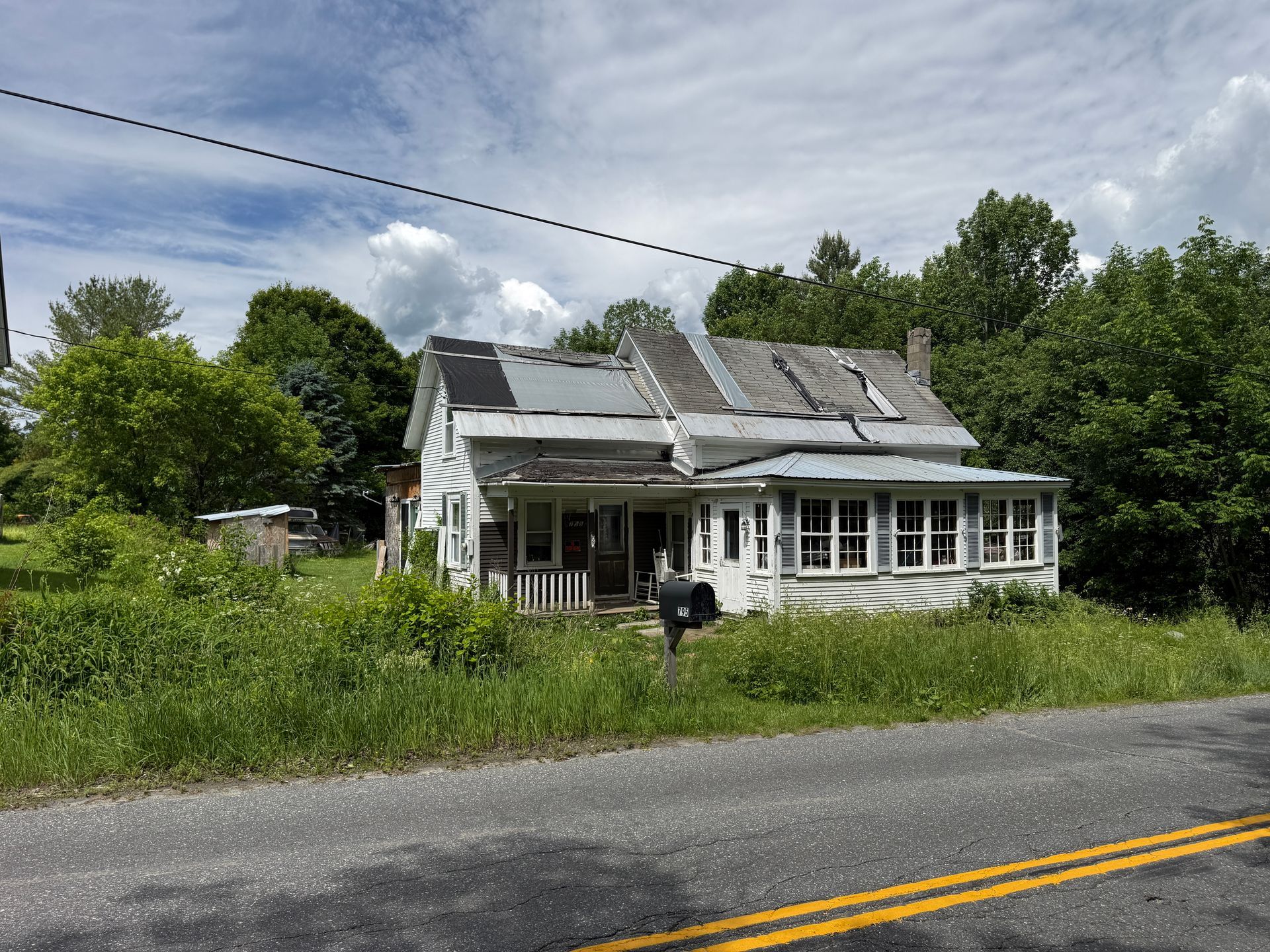 white house with a roof beside a road, grass, and trees under a cloudy sky
