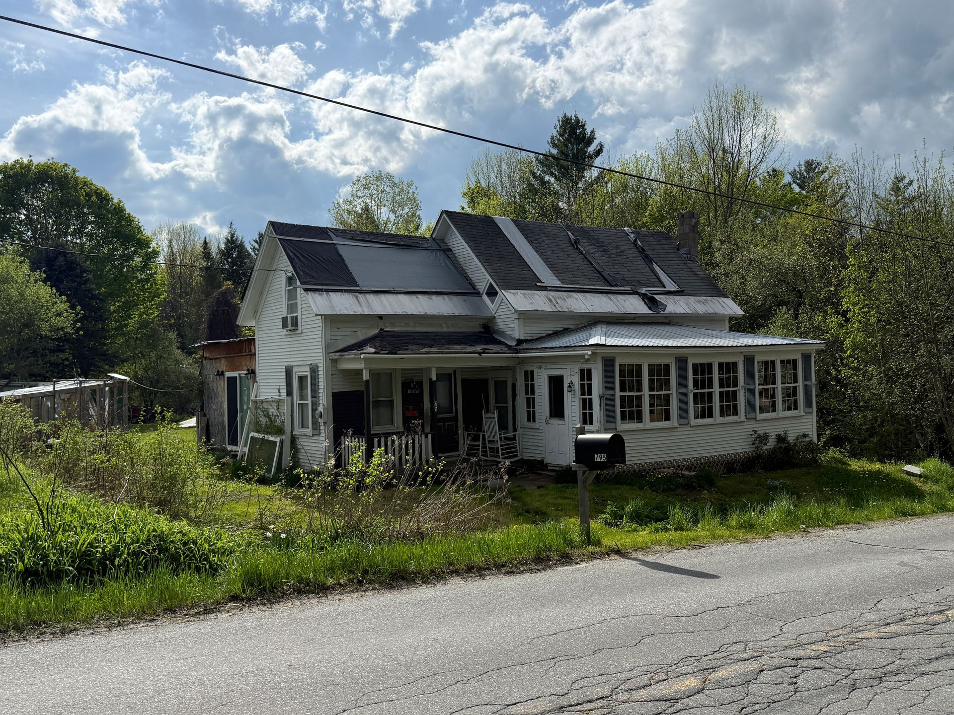 Small rural house with solar panels, white porch, and yard beside a road under a cloudy sky