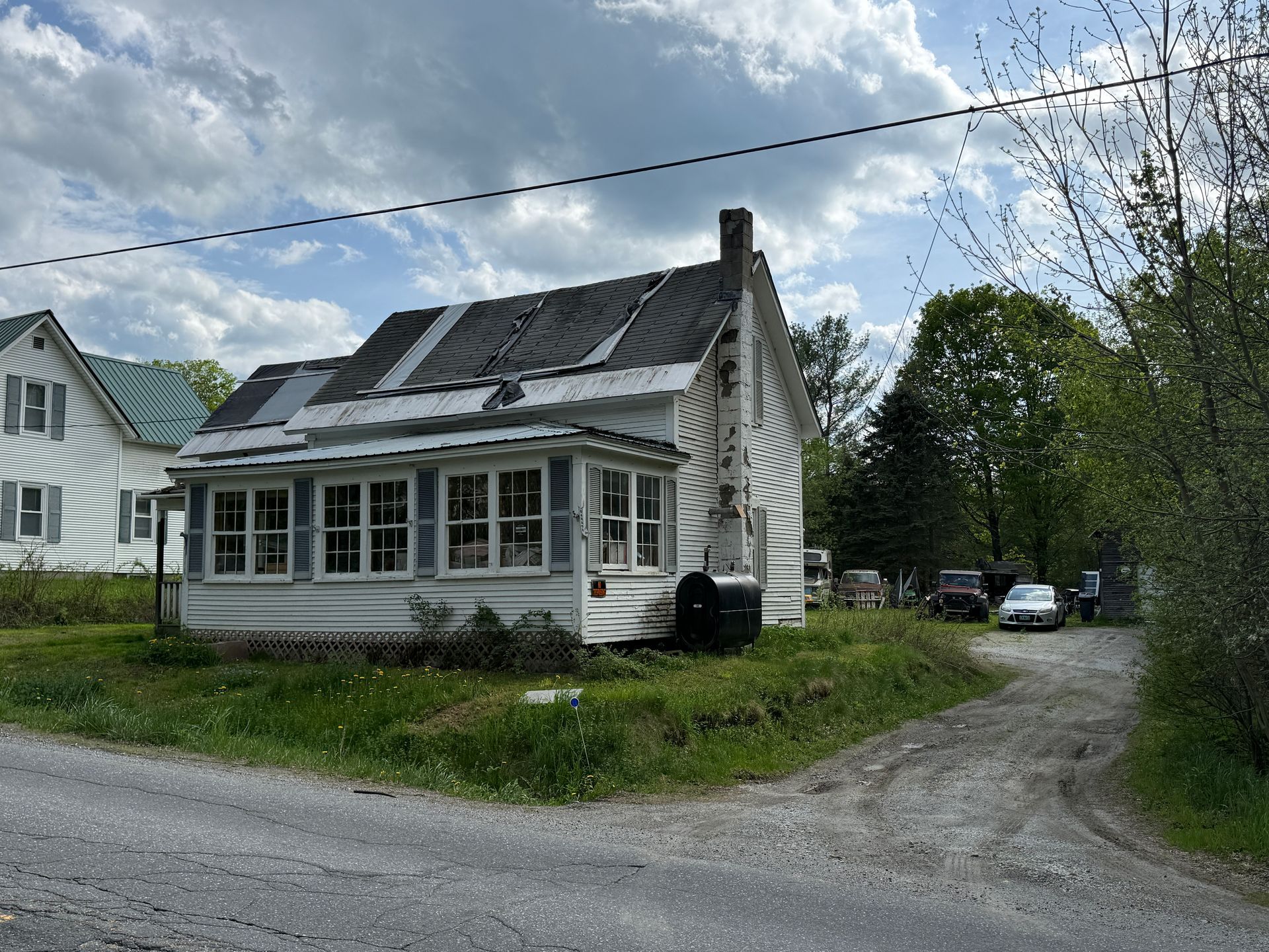 Old white house with a  roof beside a gravel road under a cloudy sky