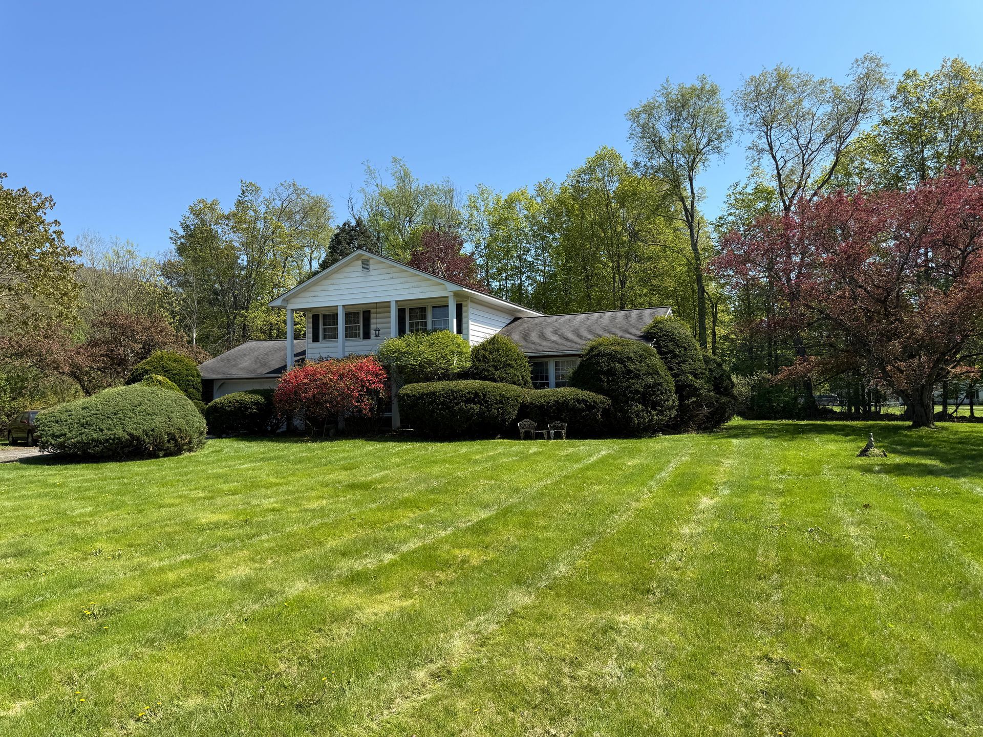 House with white exterior, green lawn, and trees. Bright, sunny day.