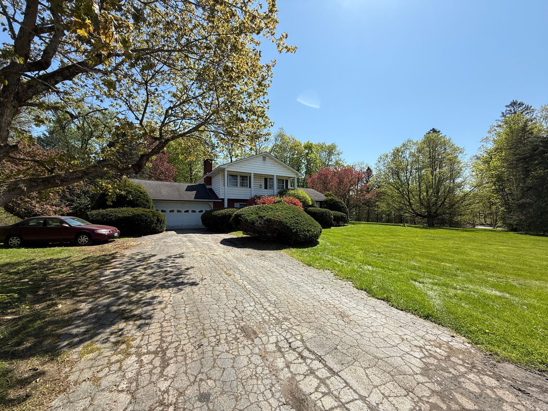 A two-story white house with a driveway, lawn, and red car on the left under a bright blue sky.