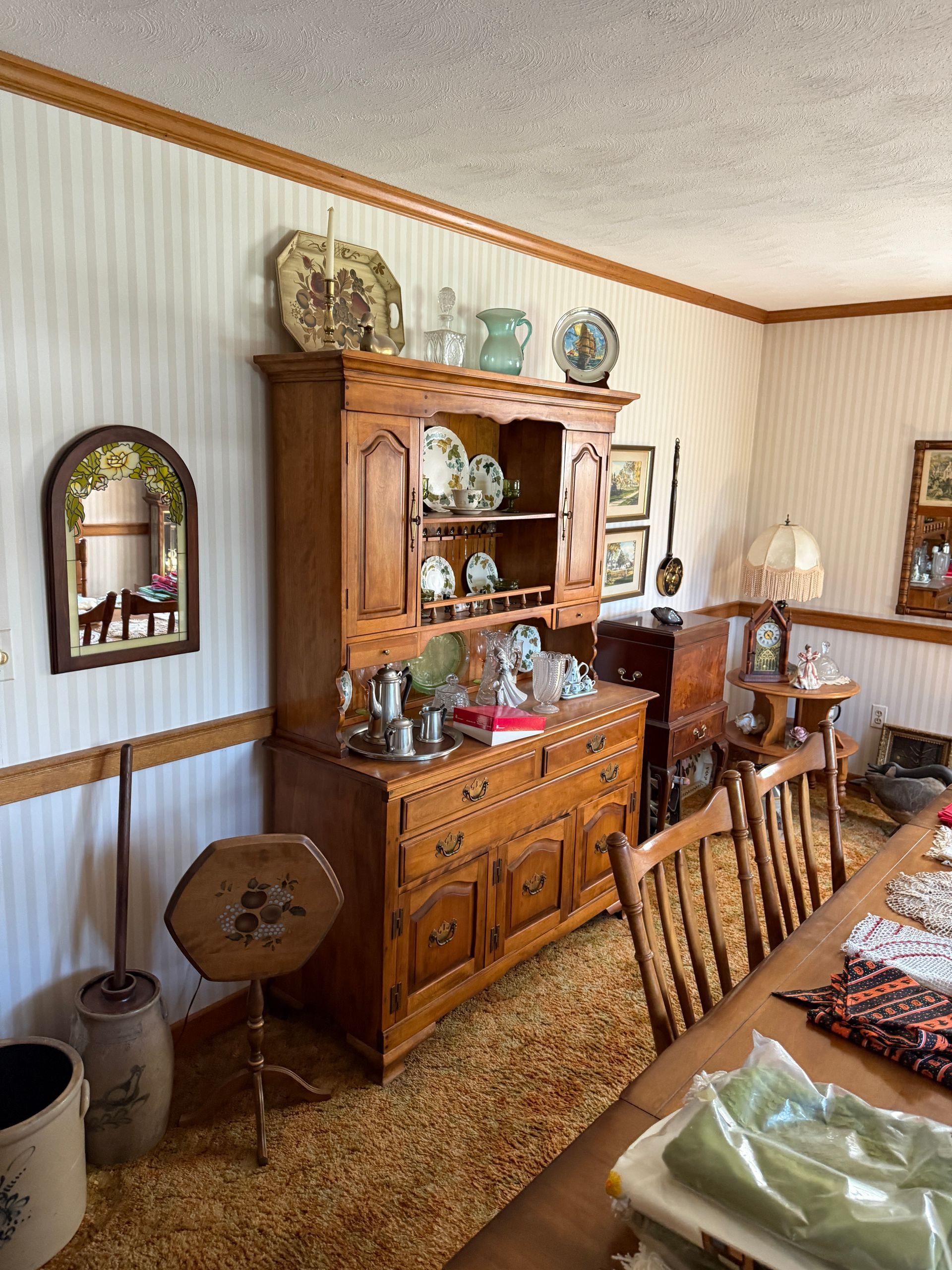 A wooden hutch with china, table, chairs, and decor in a room with patterned wallpaper.