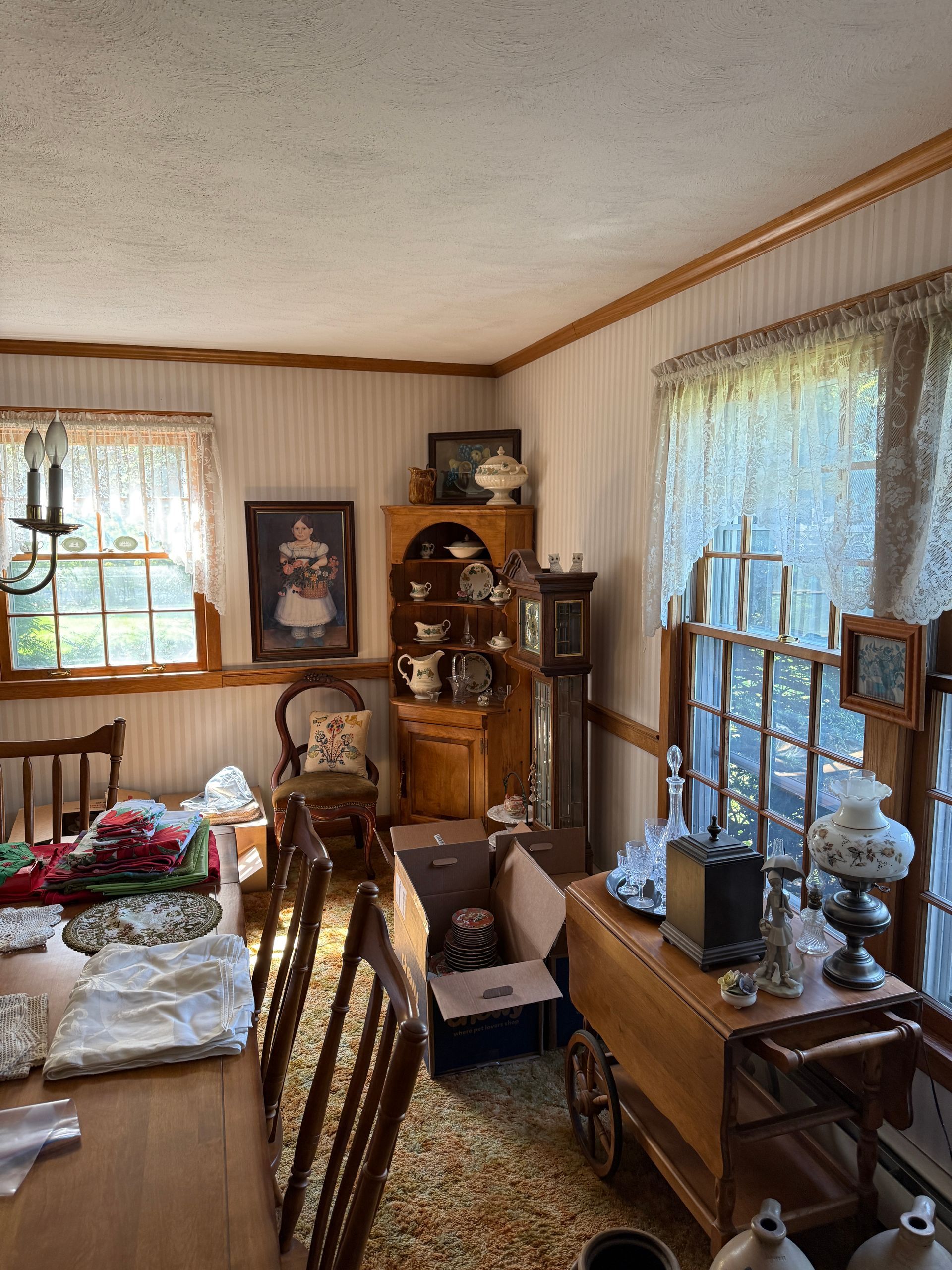 Dining room with furniture, including a corner cabinet, table, and grandfather clock near windows with curtains.