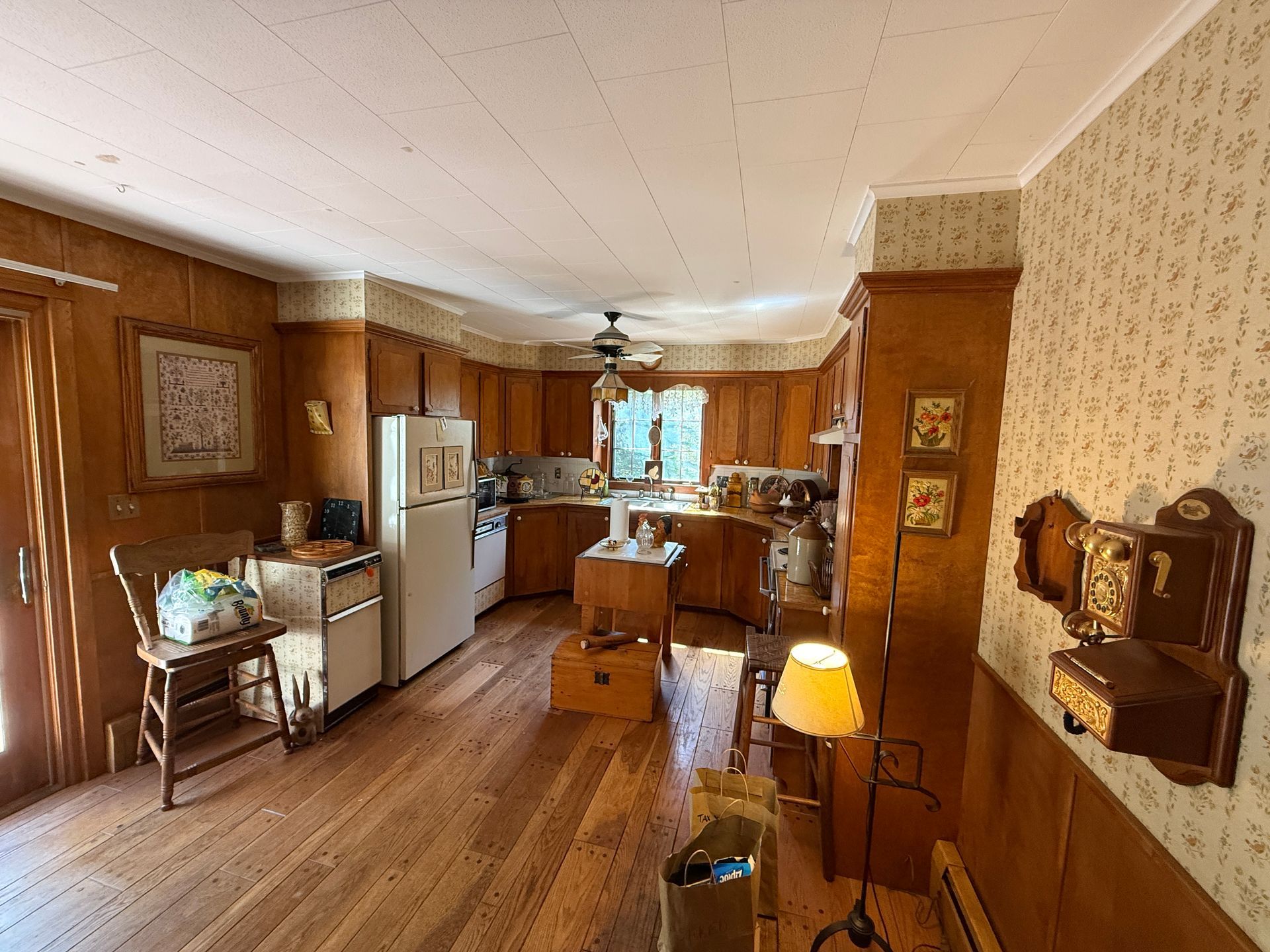 Wooden kitchen with cabinets, appliances, and island. Hardwood floors and floral wallpaper.