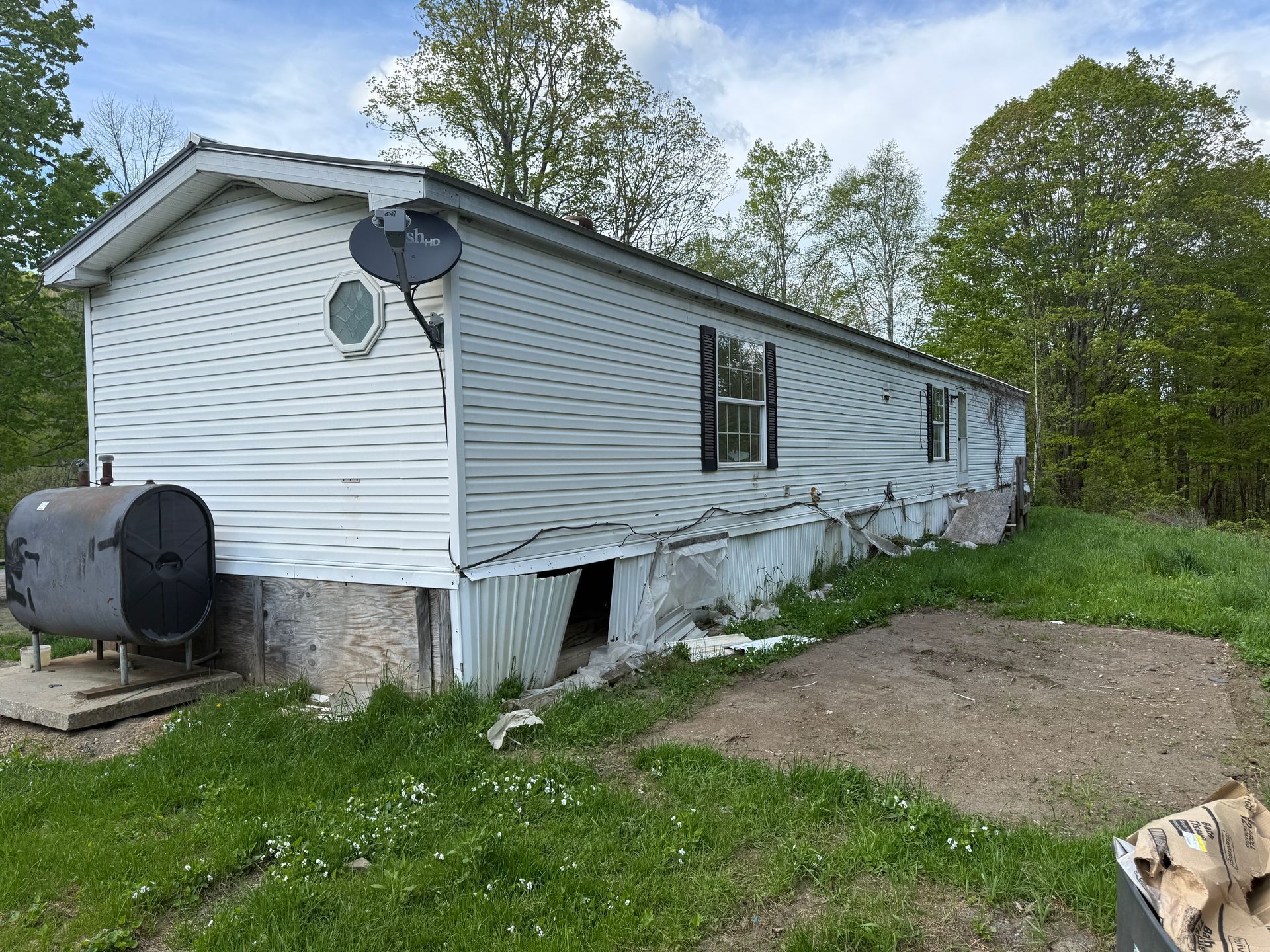 Mobile home with siding, oil tank, and satellite dish in a grassy outdoor setting.