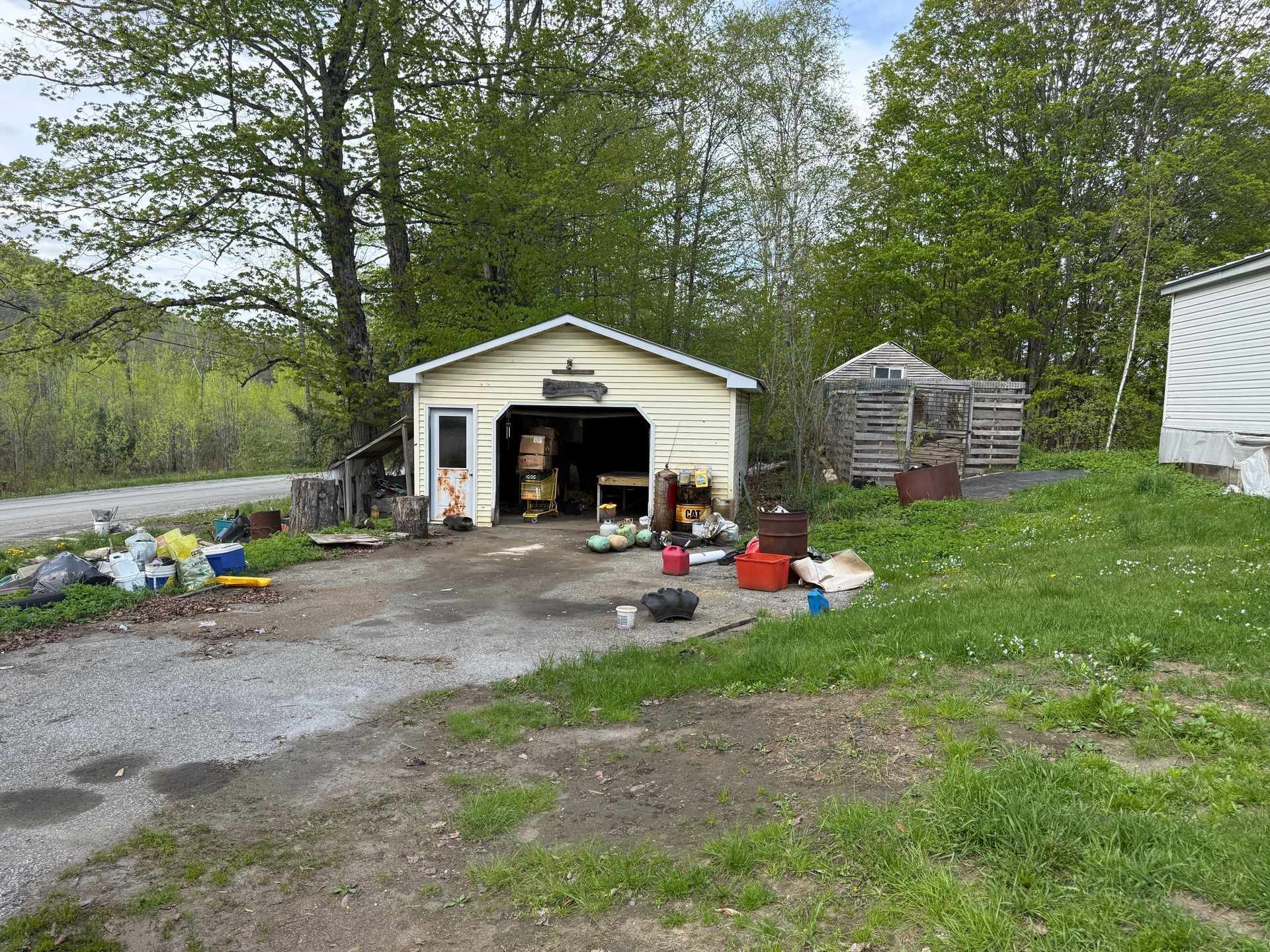 Garage with open door, gravel driveway, and surrounding trees.