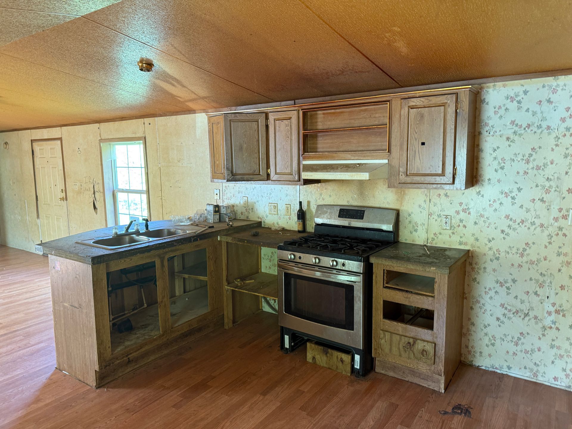 Kitchen with wooden cabinets and countertops, a gas stove, and patterned wallpaper.