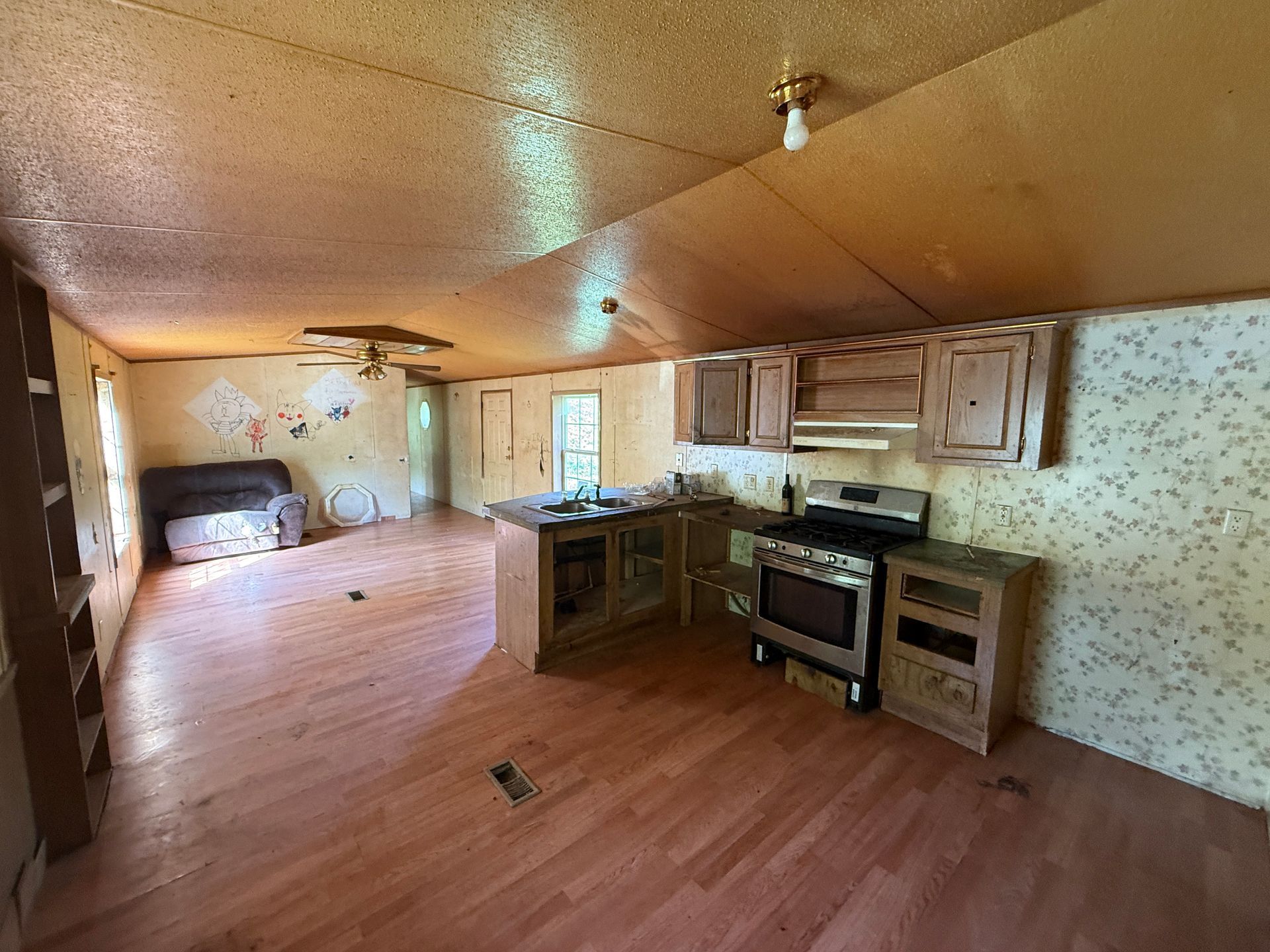 Interior of a mobile home: kitchen with oven, cabinets, and a central island; living area with furniture.