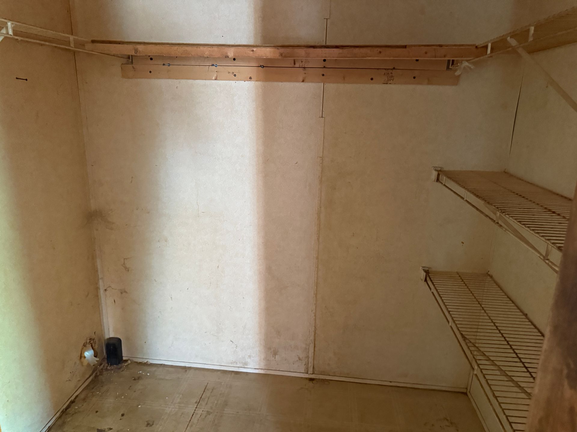Empty closet with wire shelves and wooden rod, off-white walls, and a dark floor.