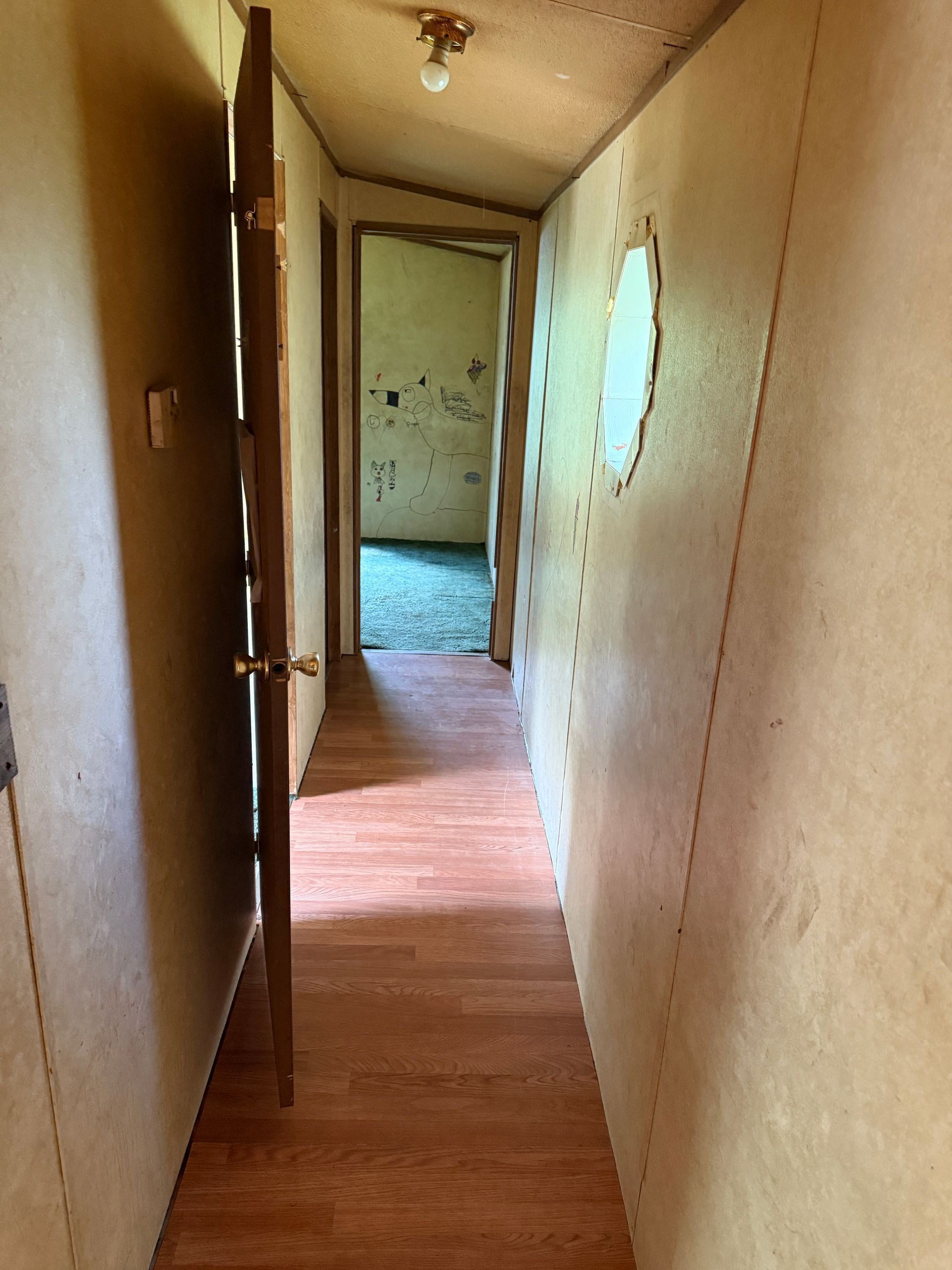 Narrow hallway with wooden floor, door open, and circular window.
