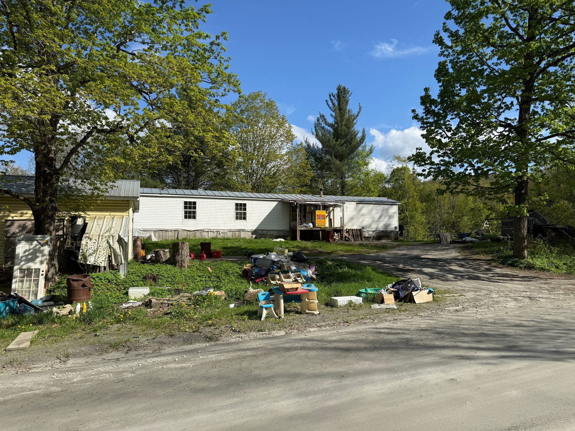 White mobile home on a grassy lot, trees, and a dirt road.