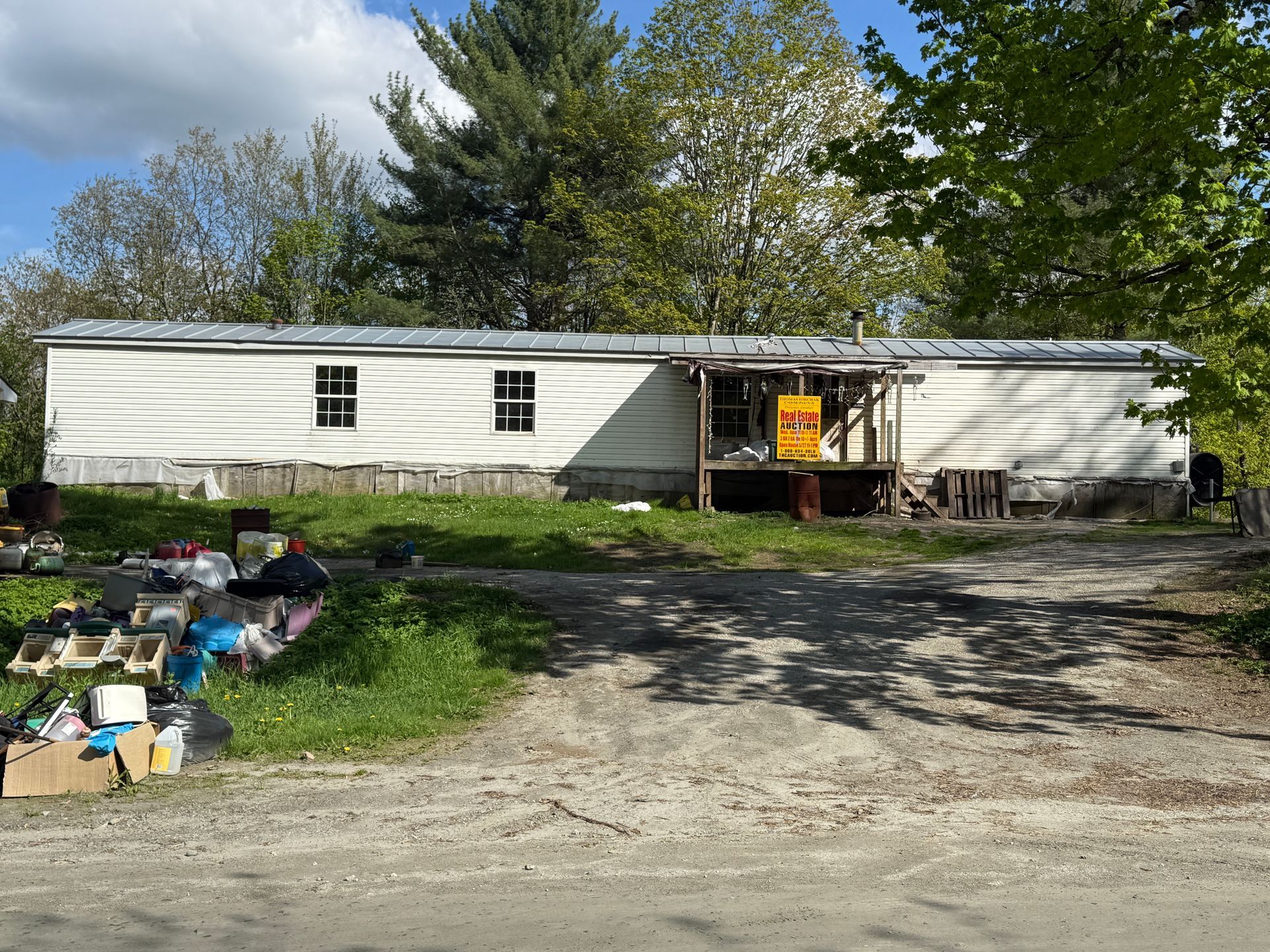 Mobile home with siding, porch, and yard, set among trees on a sunny day.