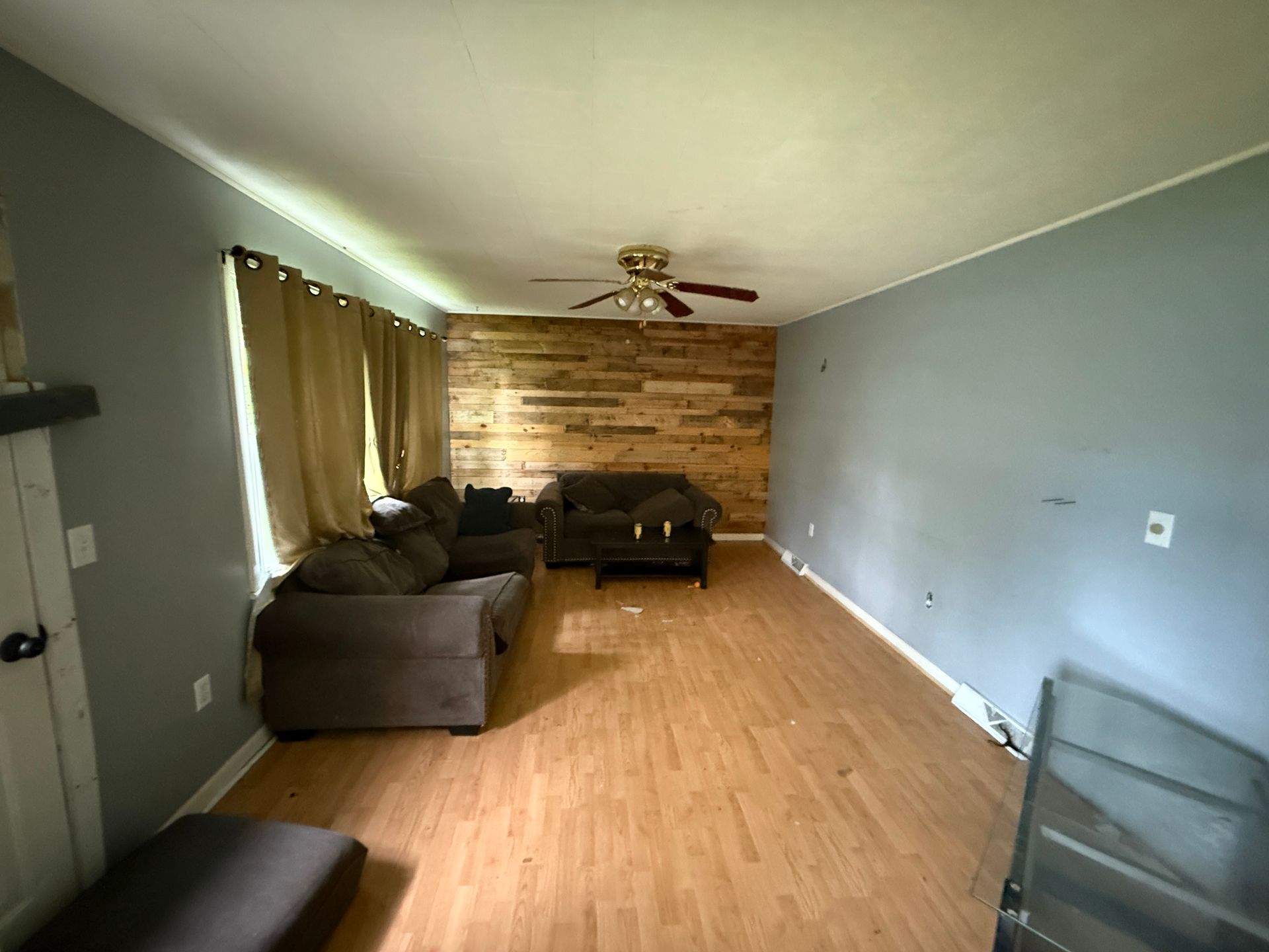 Empty living room with wood plank wall, blue walls, brown couches, and wood-look flooring.
