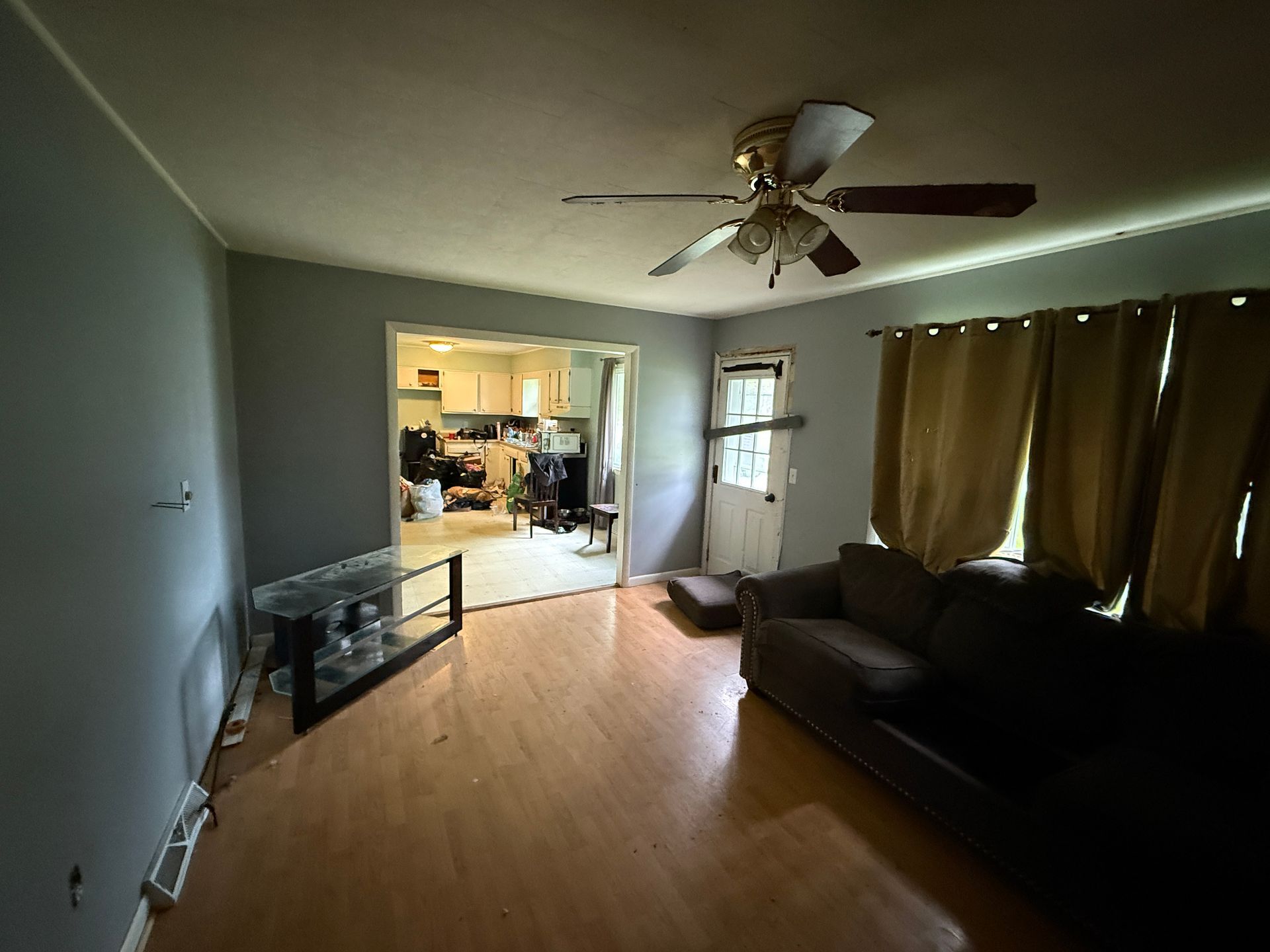 Living room with a dark sofa, light wood floors, and view into the kitchen.