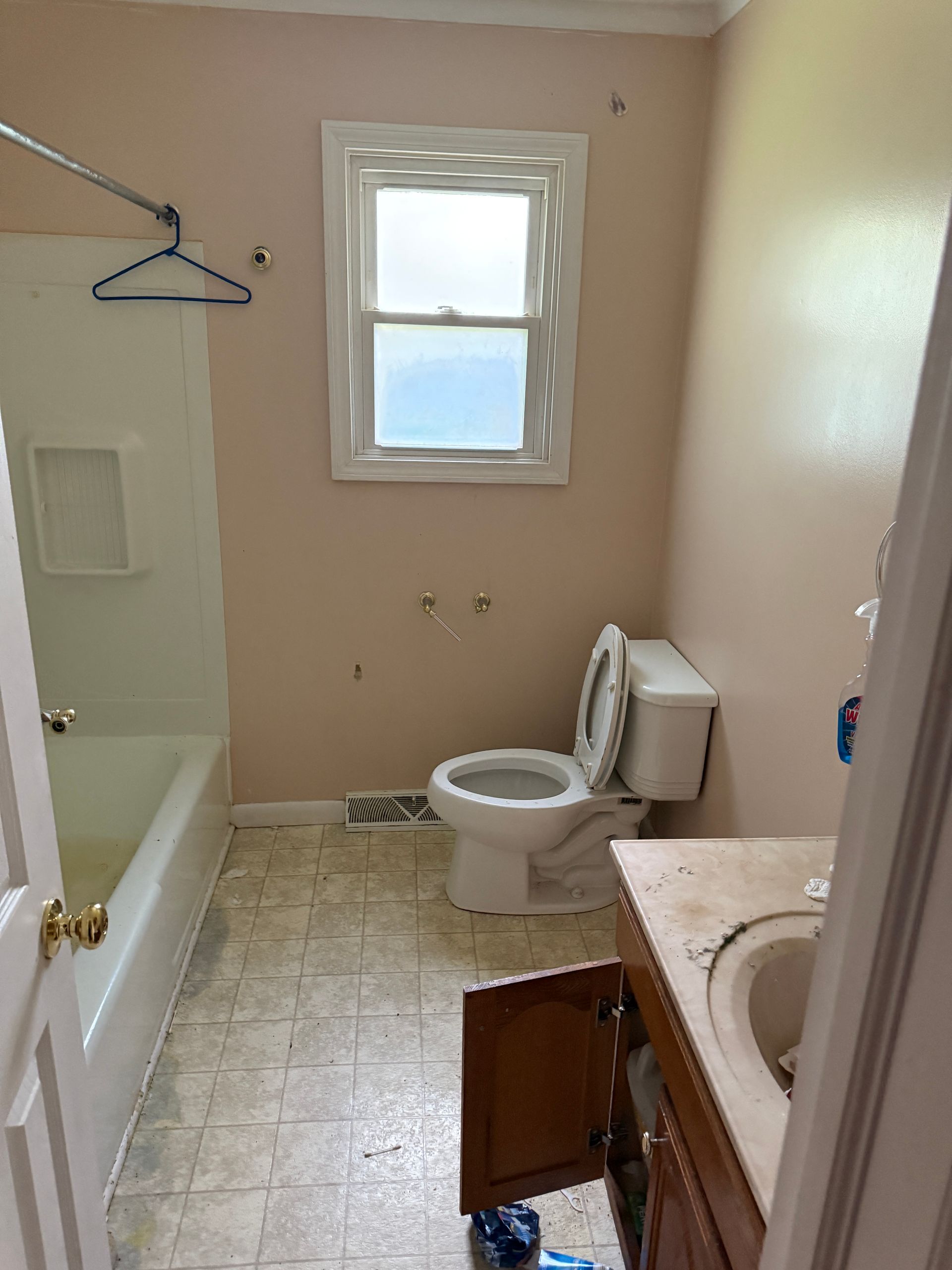 Bathroom with a white bathtub, toilet, and sink. Pink walls, a window, and a partially open cabinet.