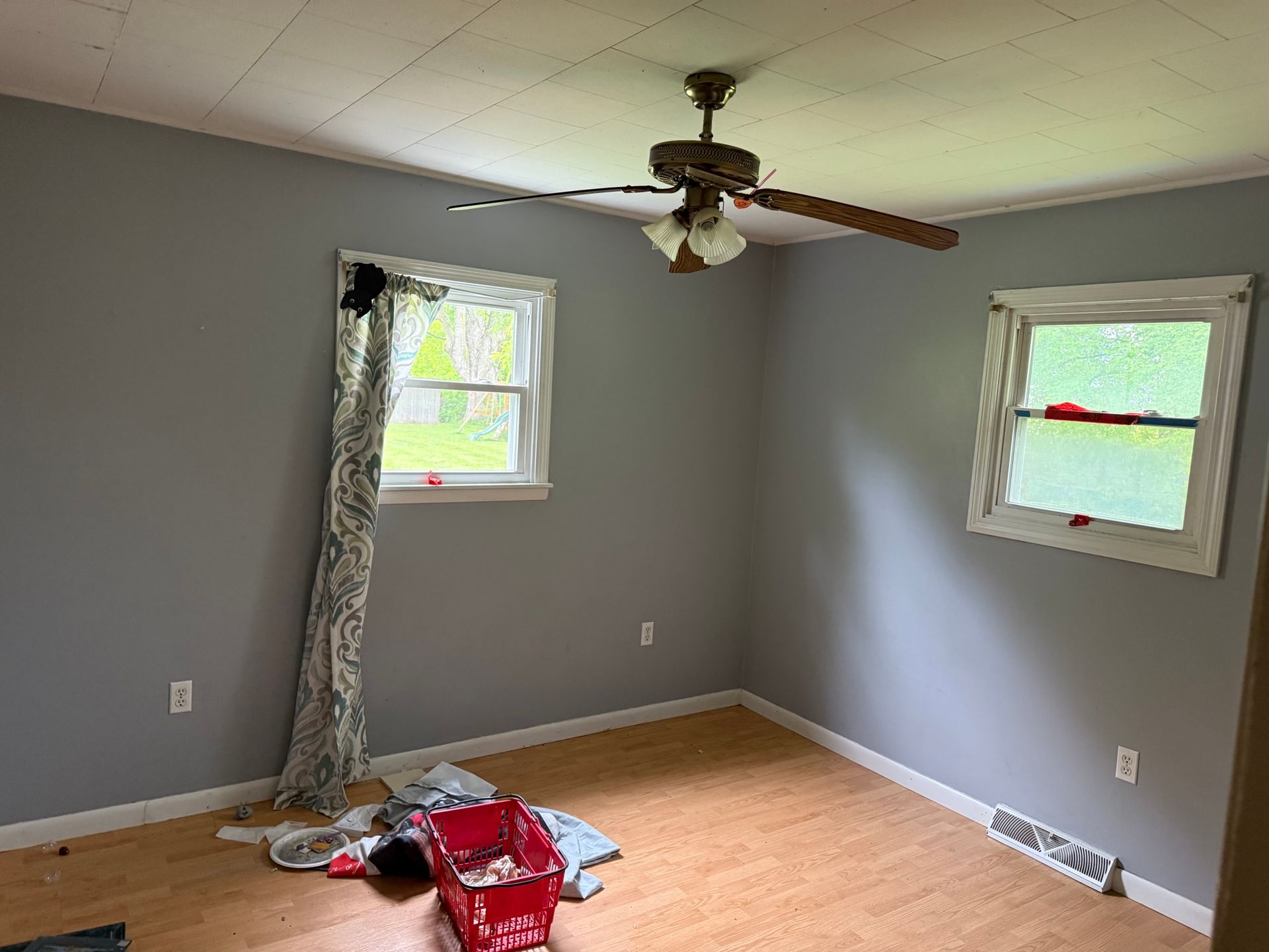 Empty room with gray walls, two windows, and a ceiling fan.