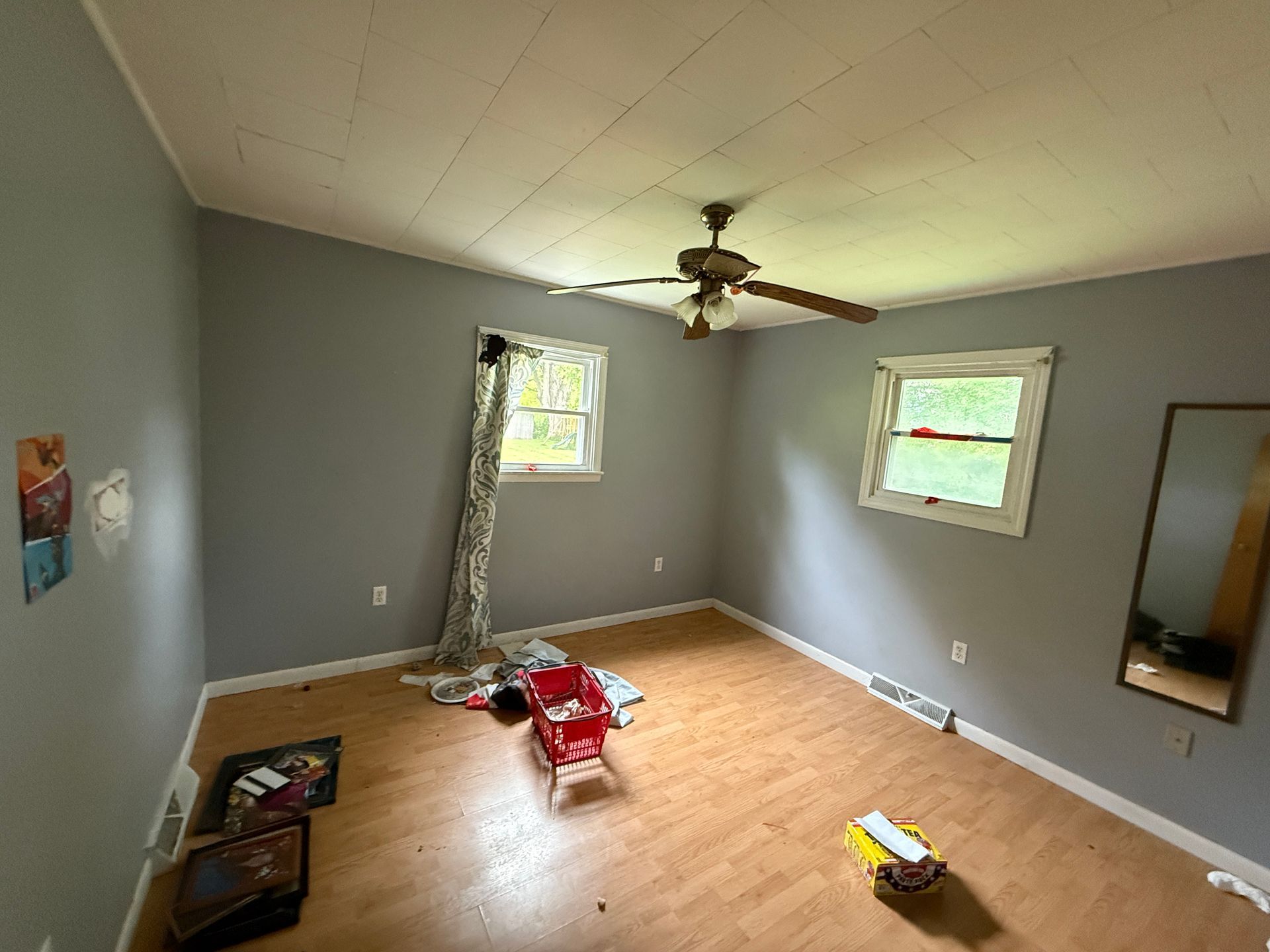 Empty room with gray walls, wood-look floor, windows, ceiling fan.