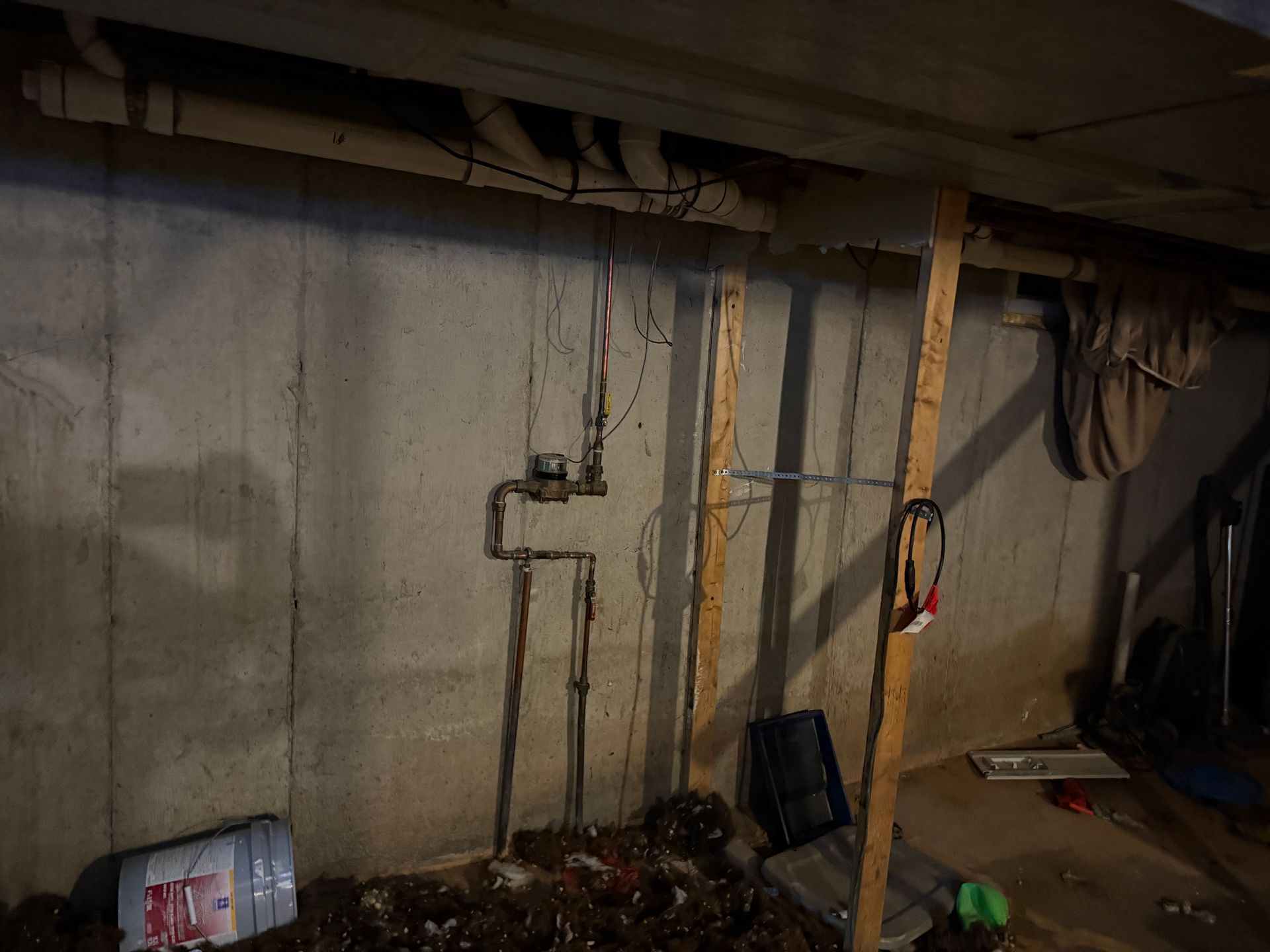 Basement wall with pipes, a wooden beam, and a water meter.