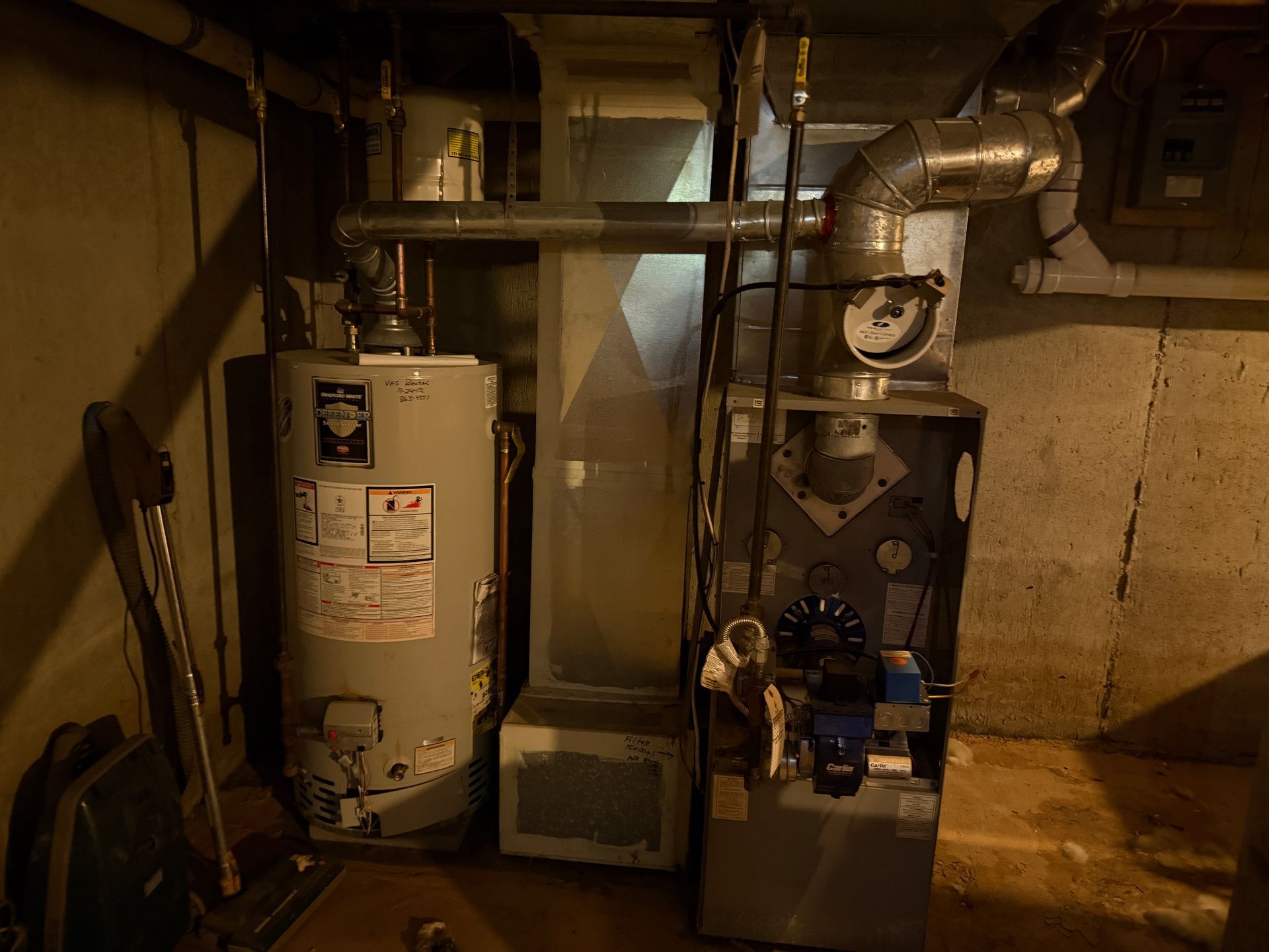 Water heater and furnace in a basement. Ductwork and pipes visible.