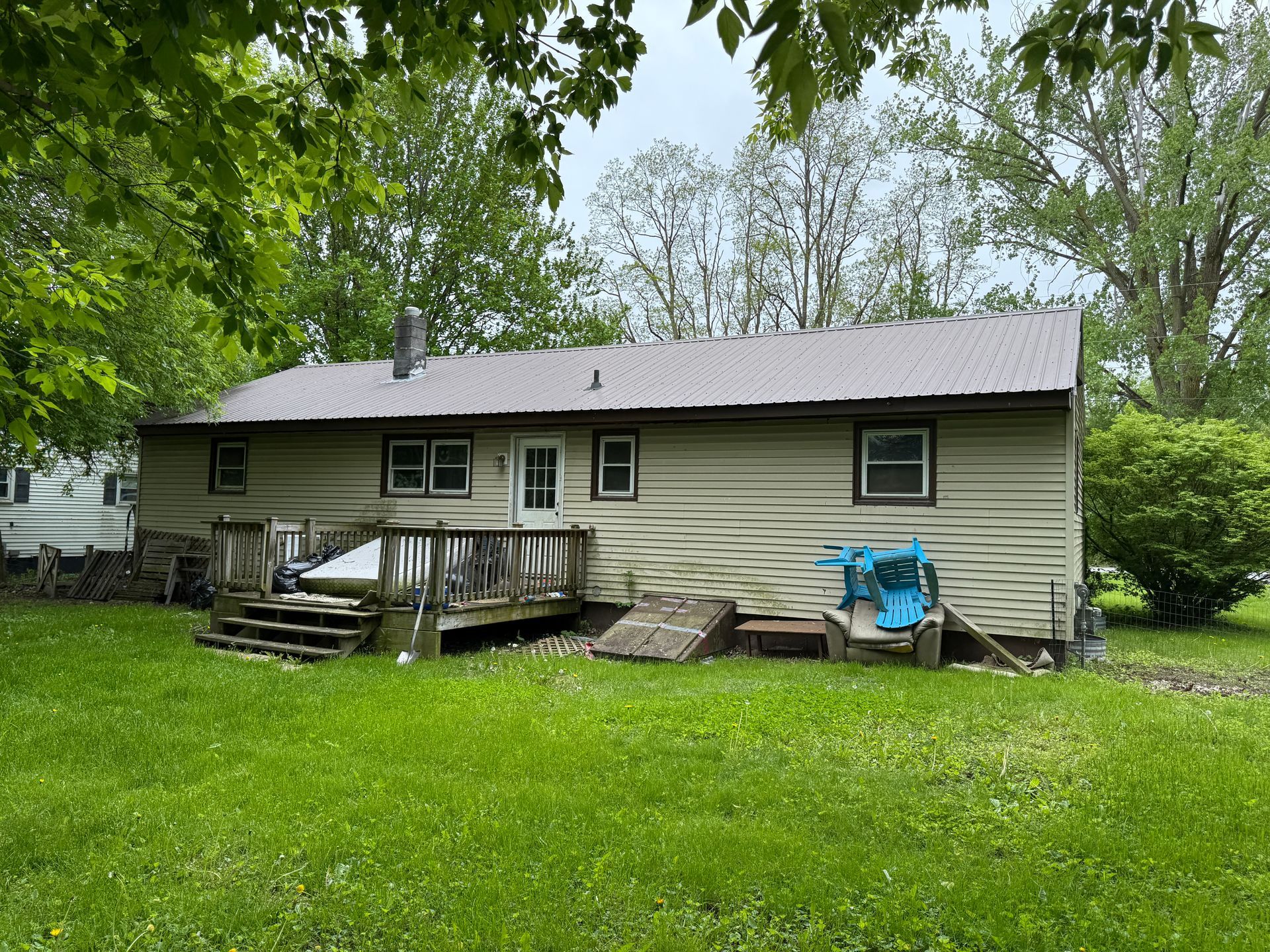Back of a tan house with a brown metal roof, a wooden deck, and a green lawn under a cloudy sky.