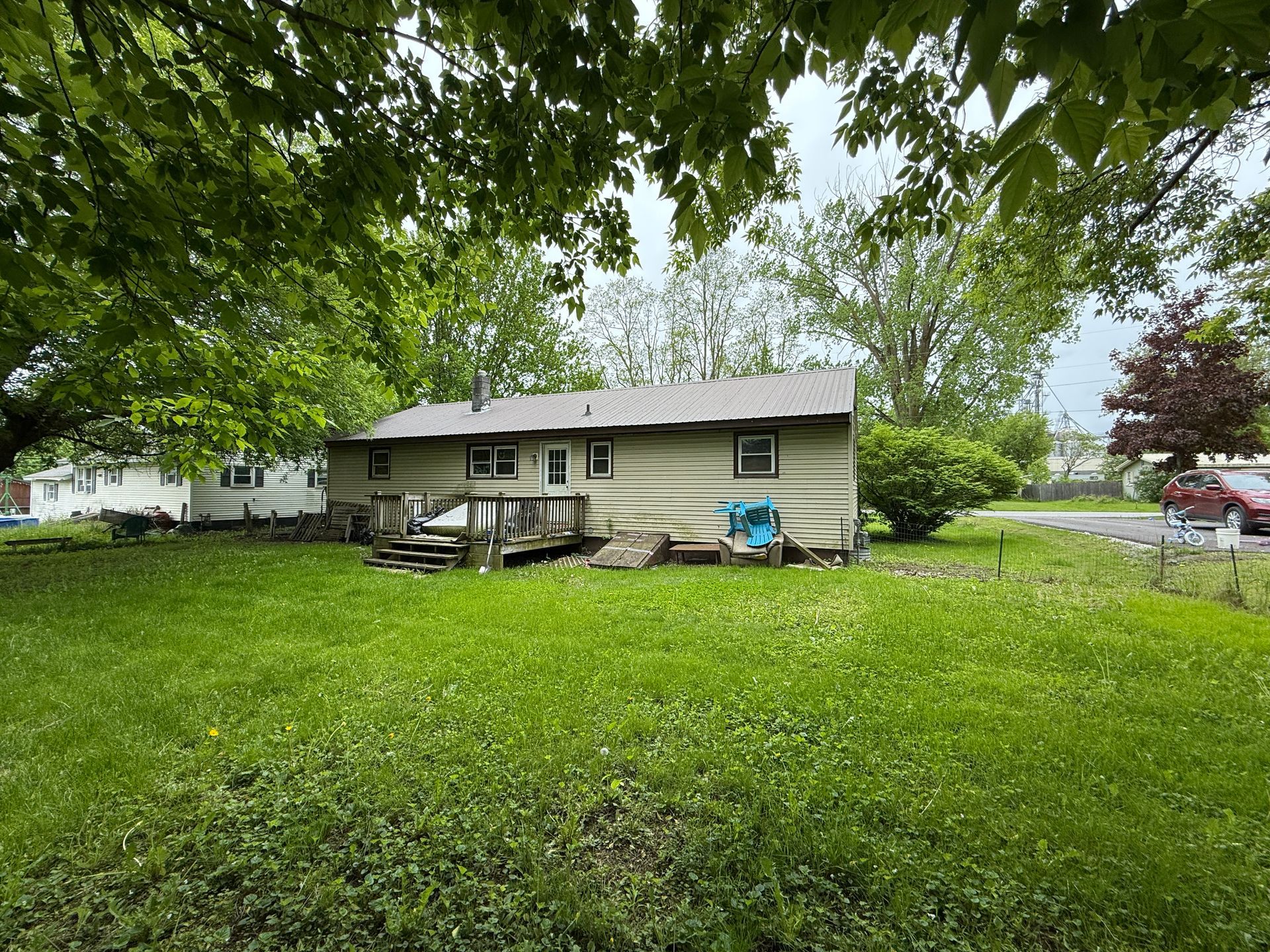Backyard view of a one-story house with a wooden deck and lawn under a cloudy sky.