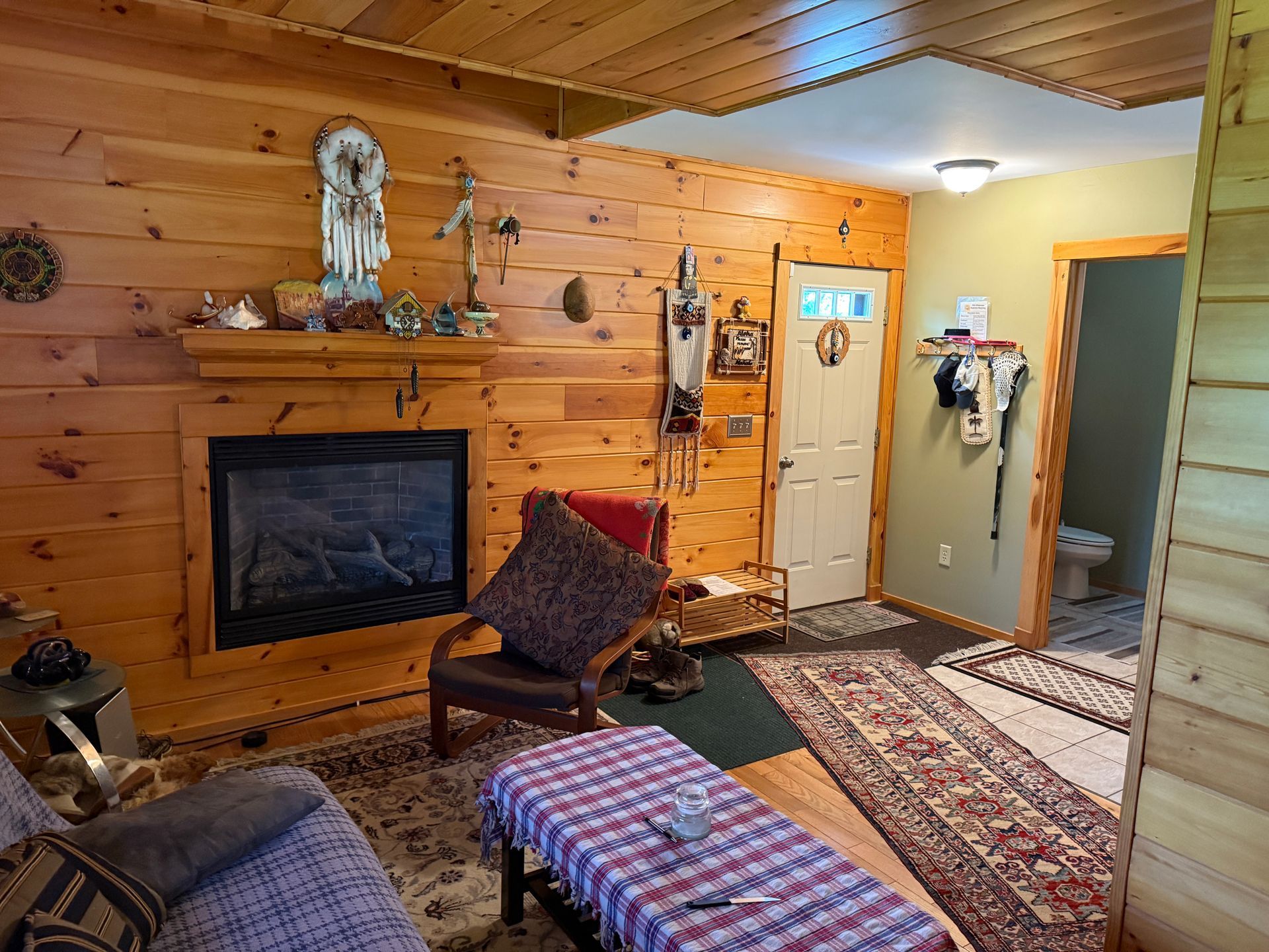 Living room with wood paneling, fireplace, rug, chair, and doorway to a bathroom.