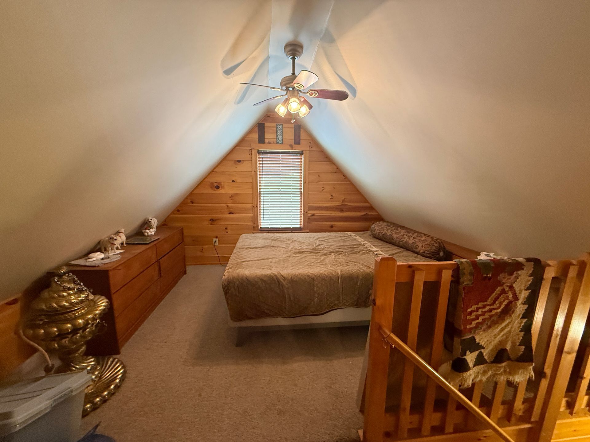Cozy attic bedroom with wooden walls, bed, dresser, and a decorative wooden stair railing.
