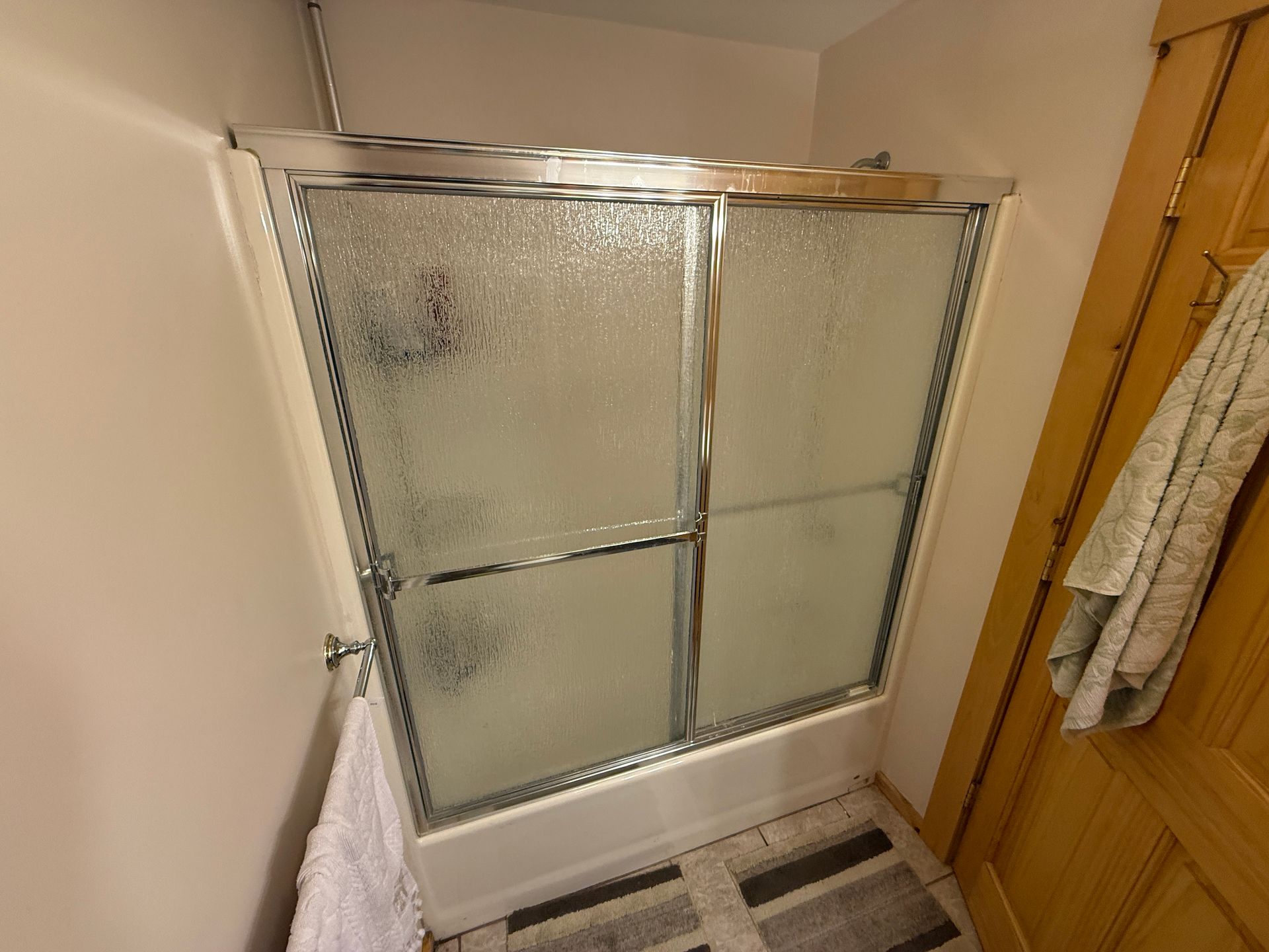 Shower with frosted glass doors, towel rack with towel, and wooden door.