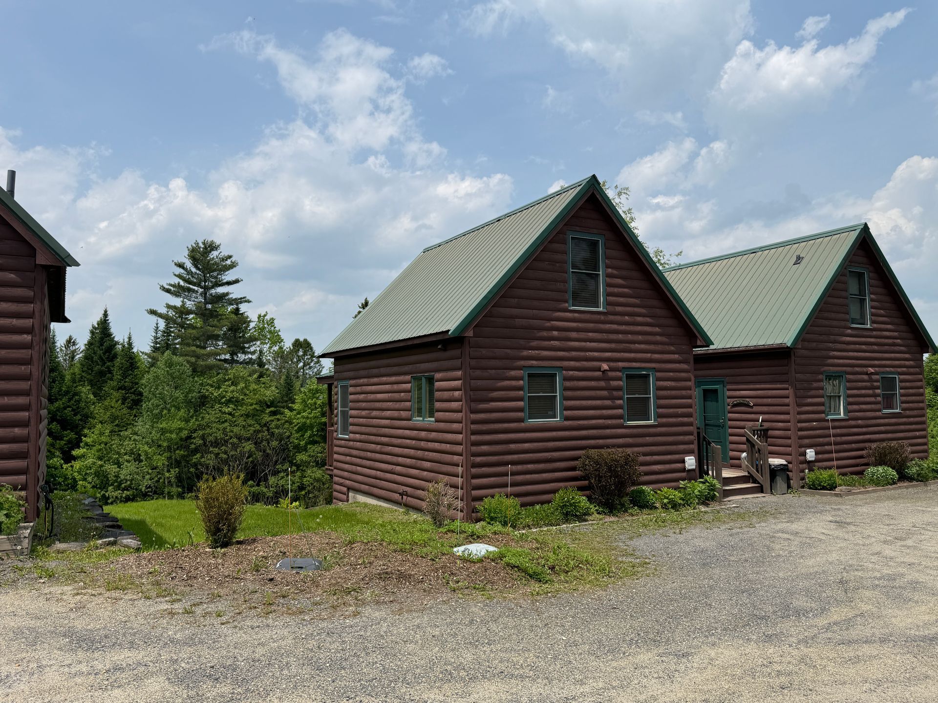 Brown log cabins with green roofs and windows under a partly cloudy sky.