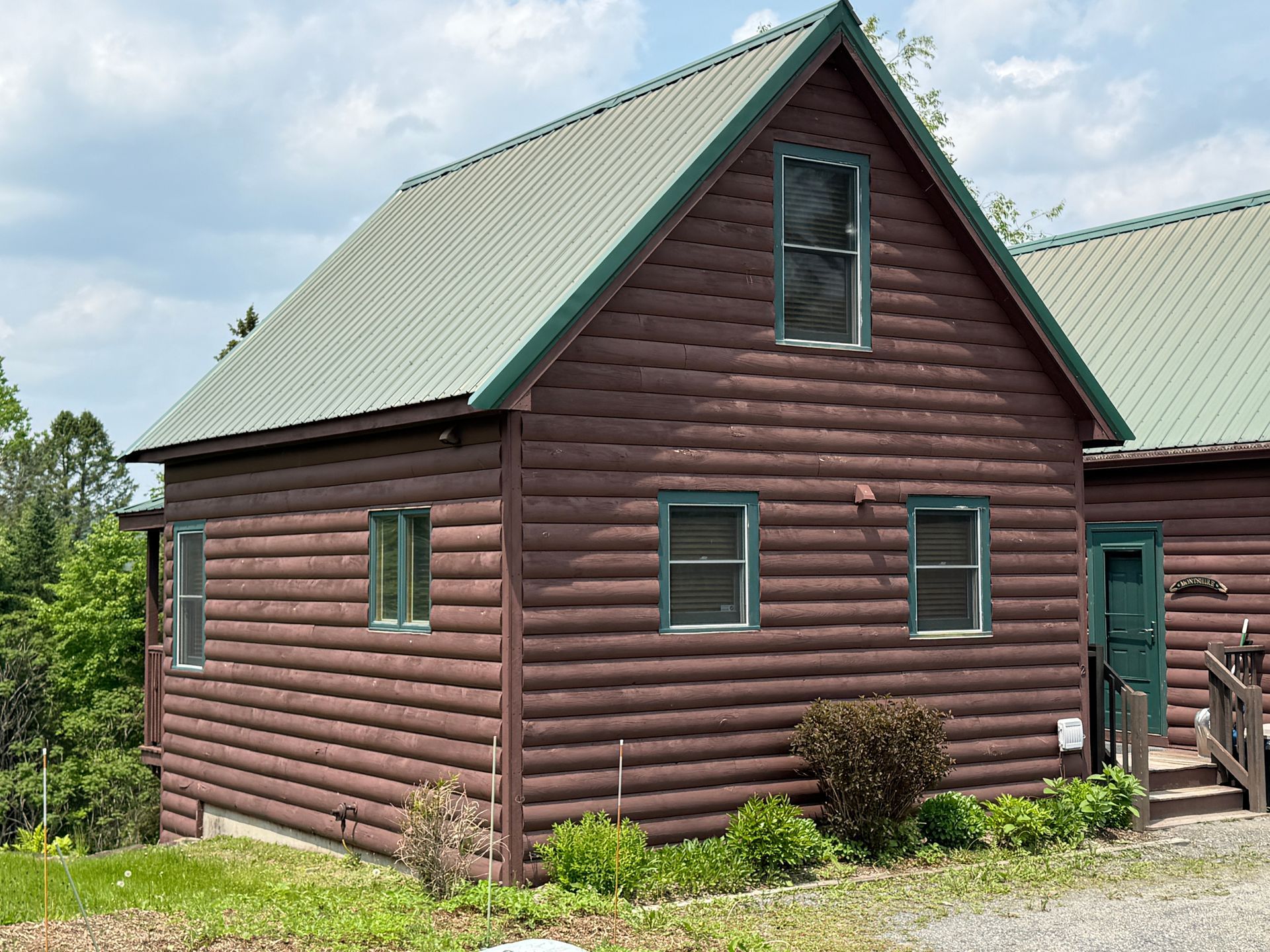 Brown cabin with green trim and roof. Windows and door visible. Cloudy sky.