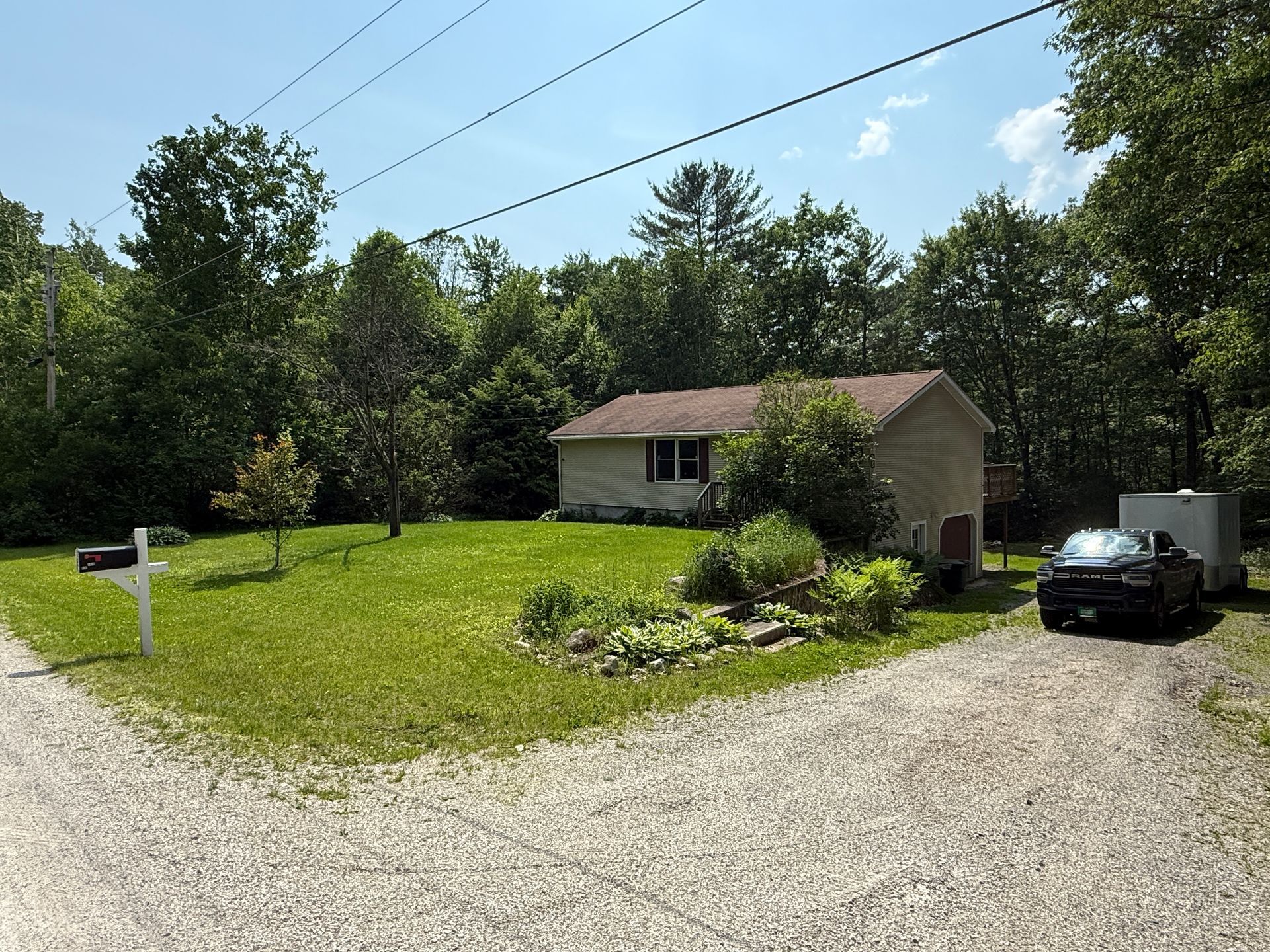 Small house with green lawn, mailbox, and gravel driveway.