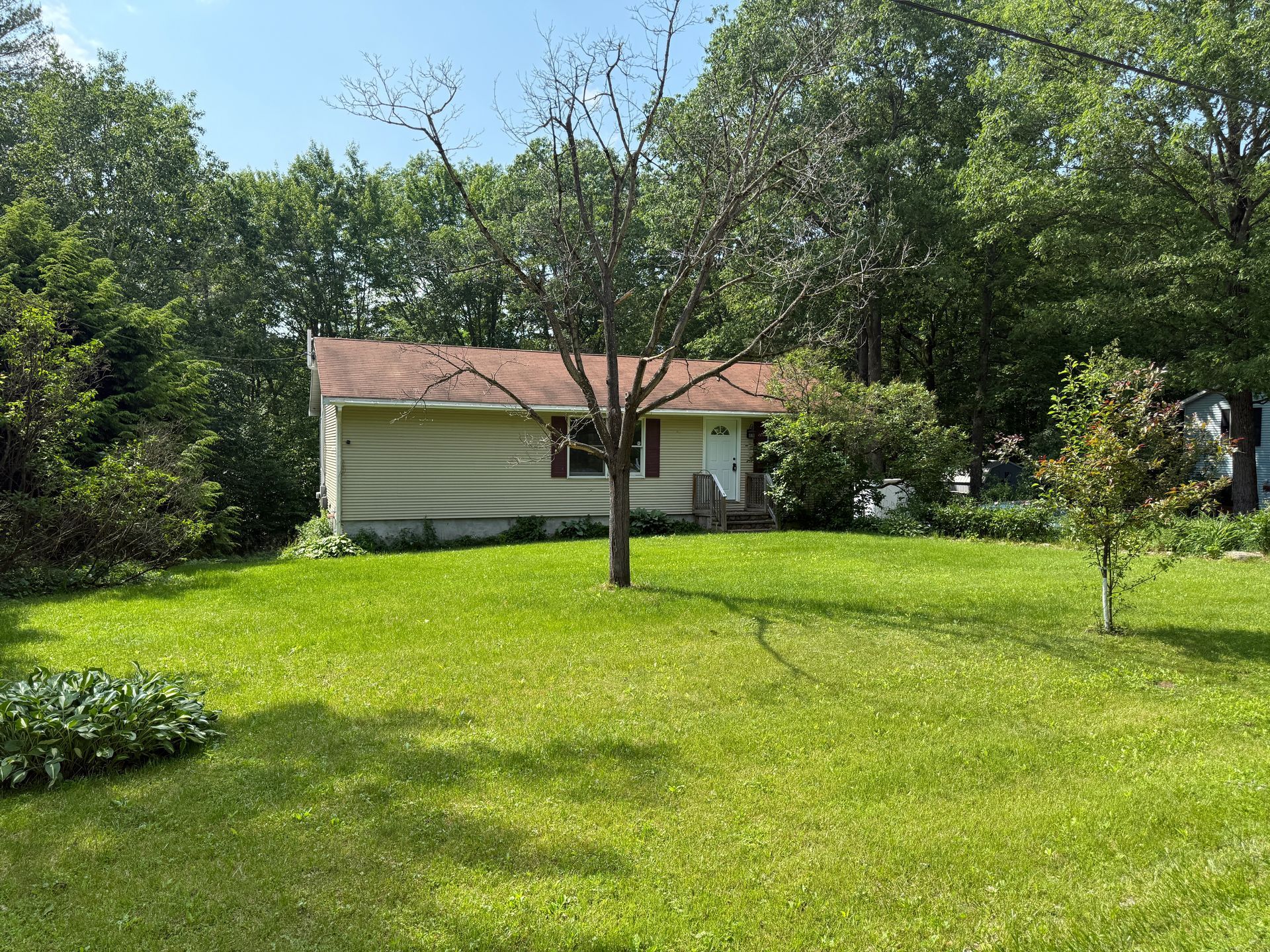 Small house with brown roof, surrounded by green grass and trees.