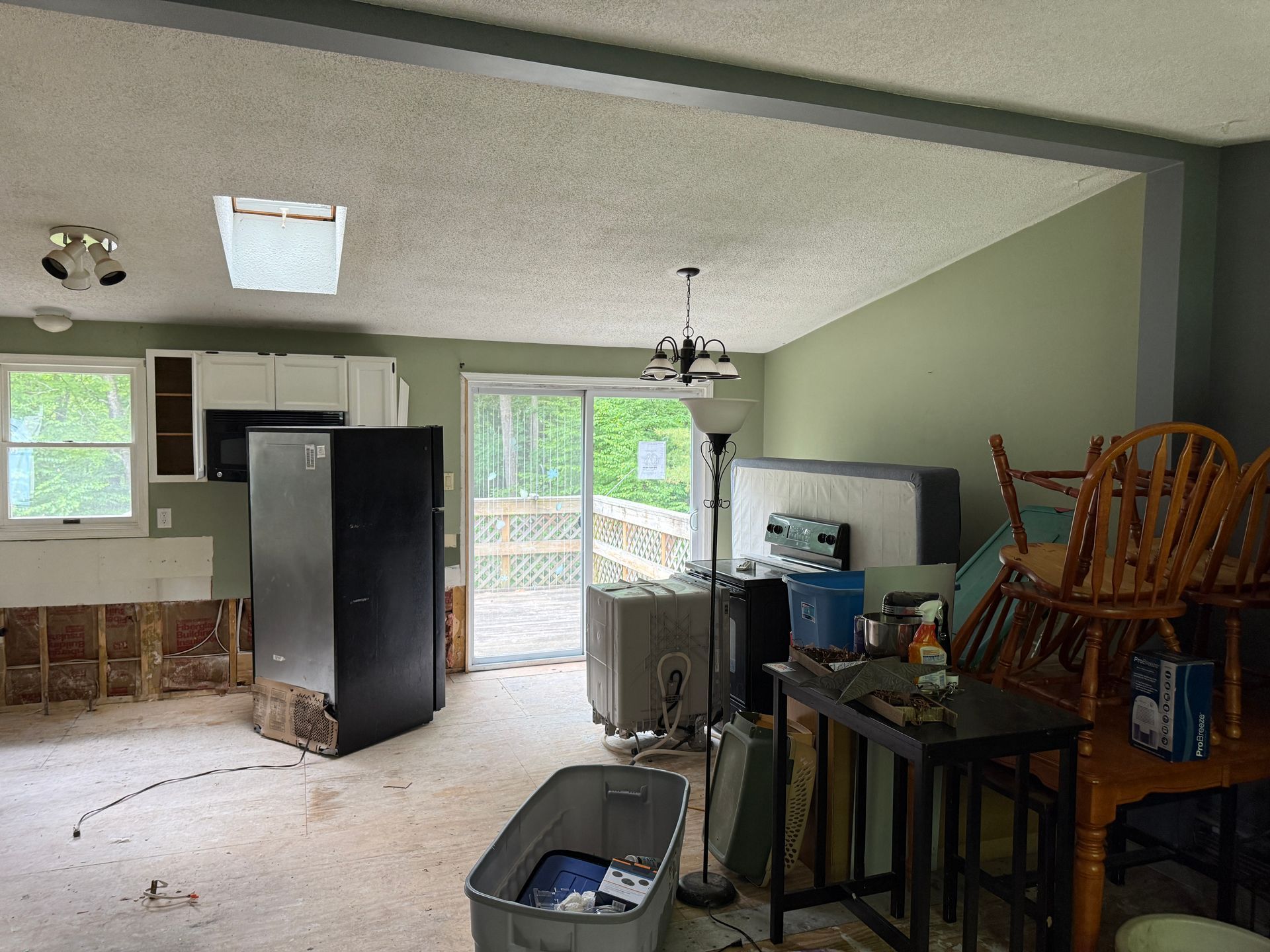 Interior view of a room with exposed wall, refrigerator, and a sliding door leading to a deck.