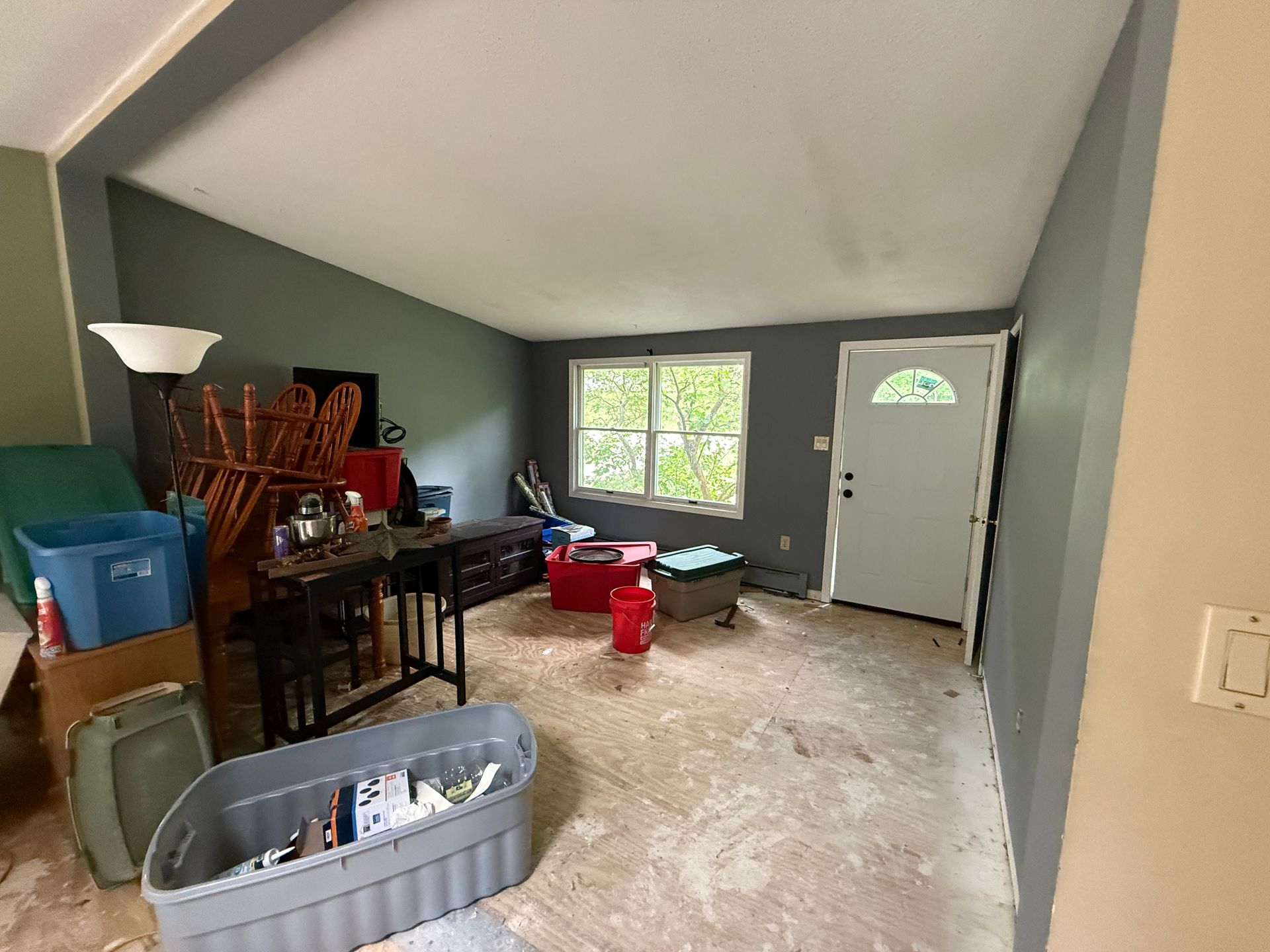 Room with gray walls, window, door, and various storage bins and furniture.