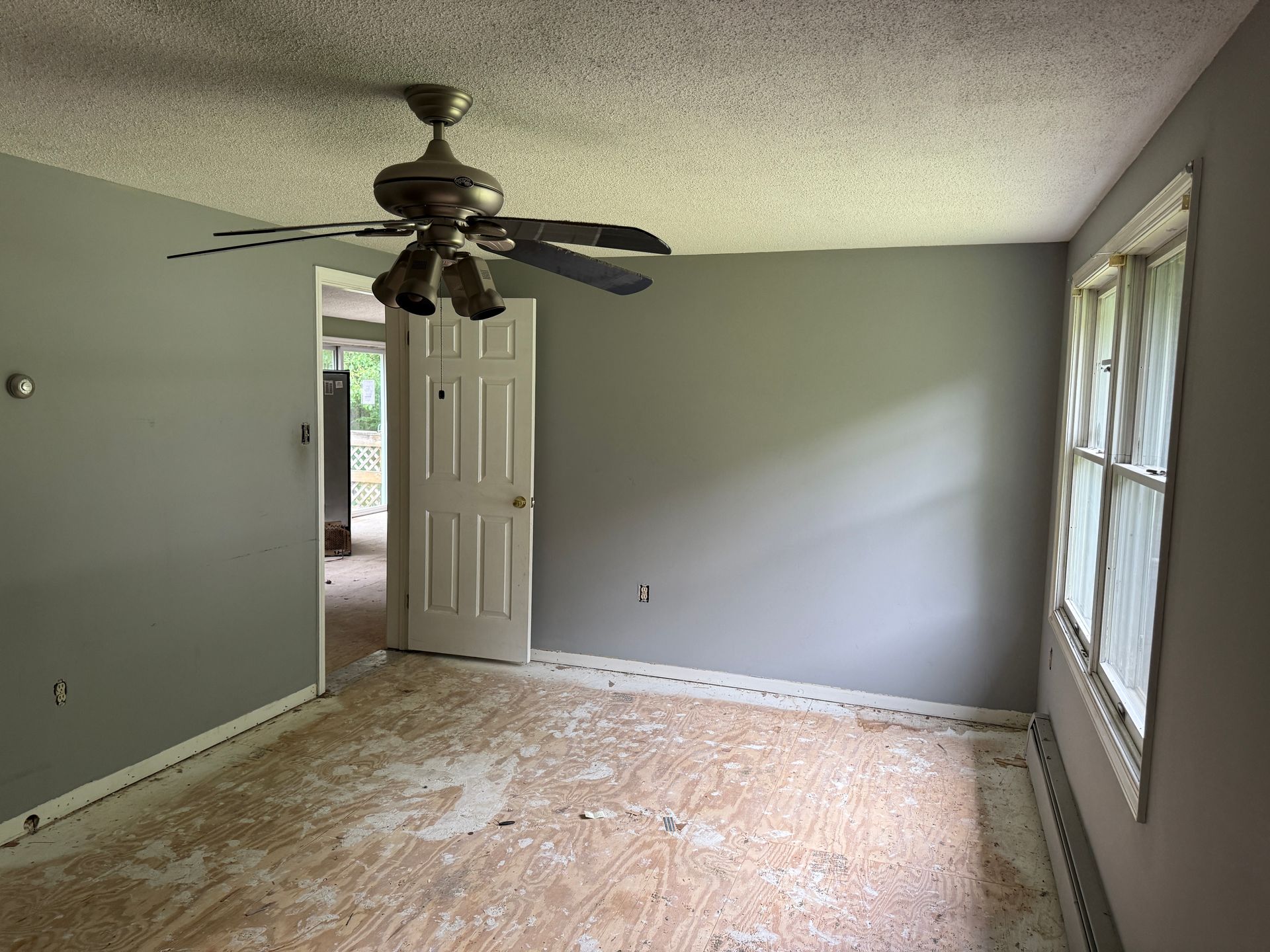 Empty room with gray walls, white door, ceiling fan, and window.