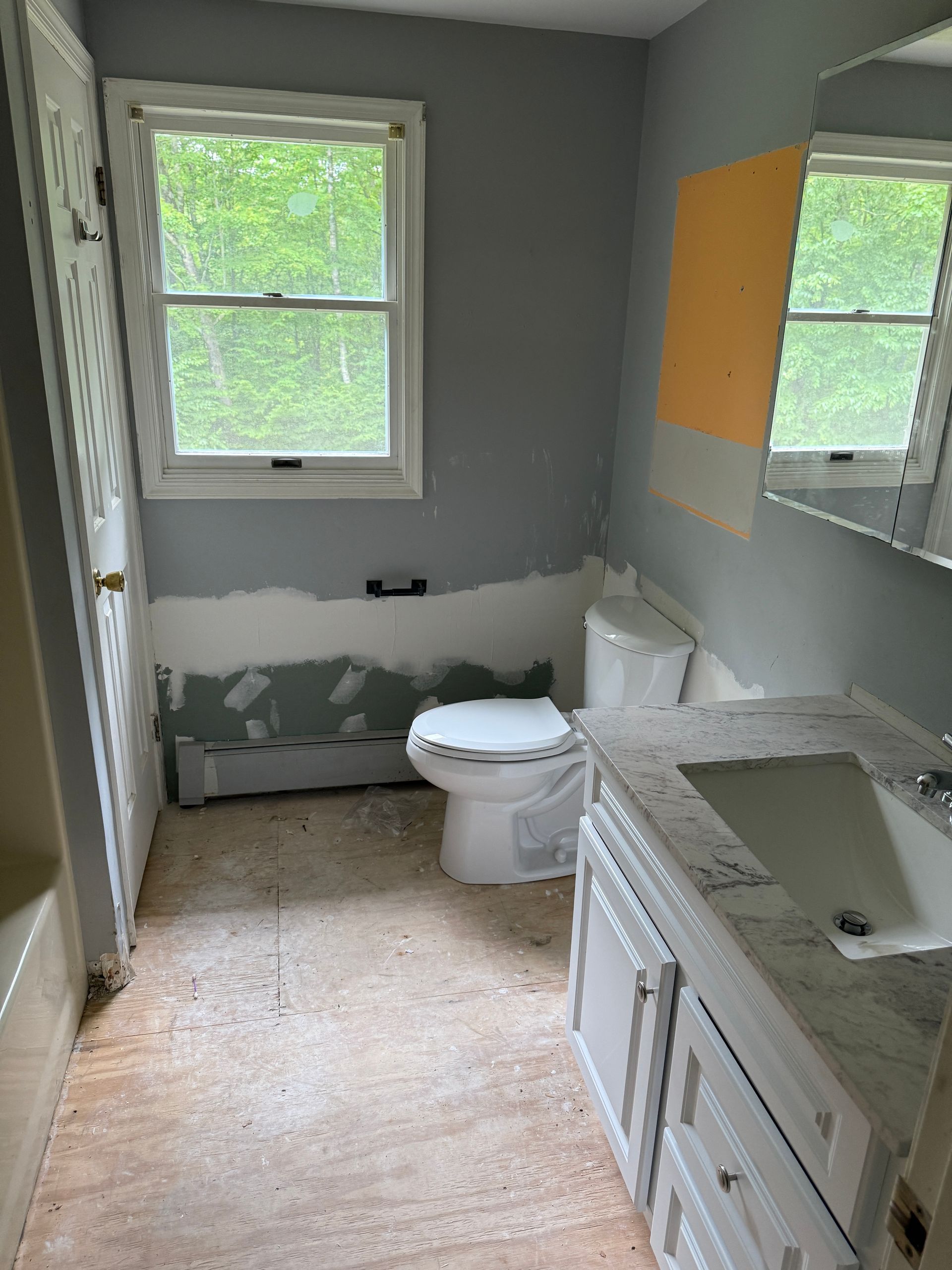 Bathroom with toilet, vanity, window, and wall. Gray walls, white toilet, tan floor.