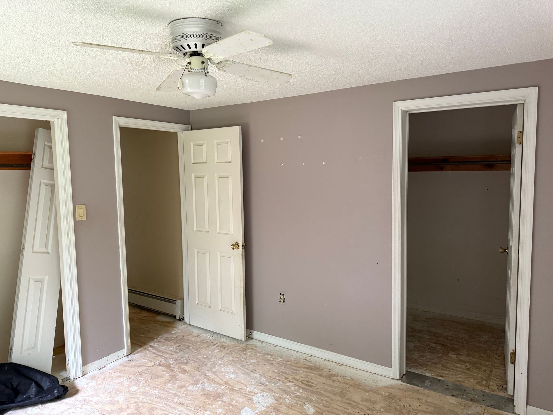 Empty room with lavender walls, white trim, three doorways, ceiling fan.