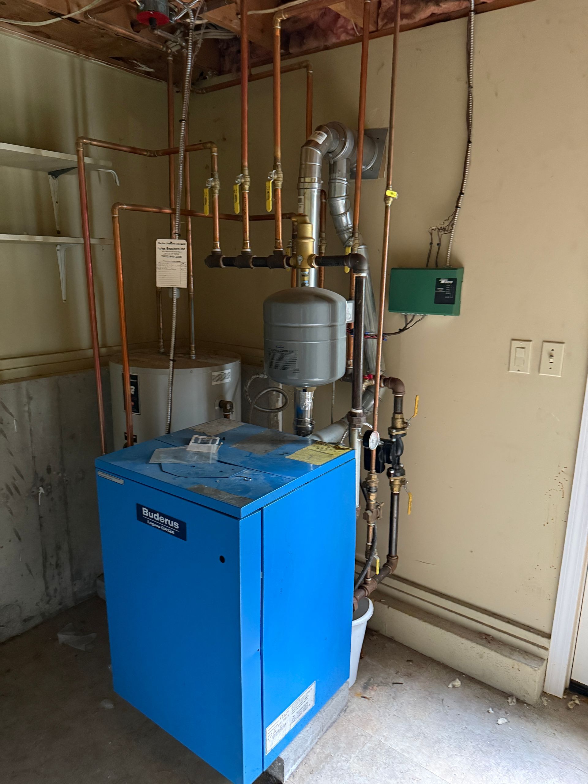 Blue boiler with copper pipes and related equipment against a beige wall.