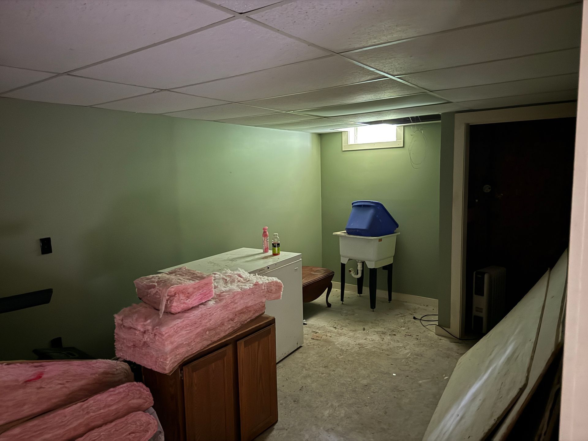 Basement with pale green walls, ceiling, laundry appliances, insulation, and small window.