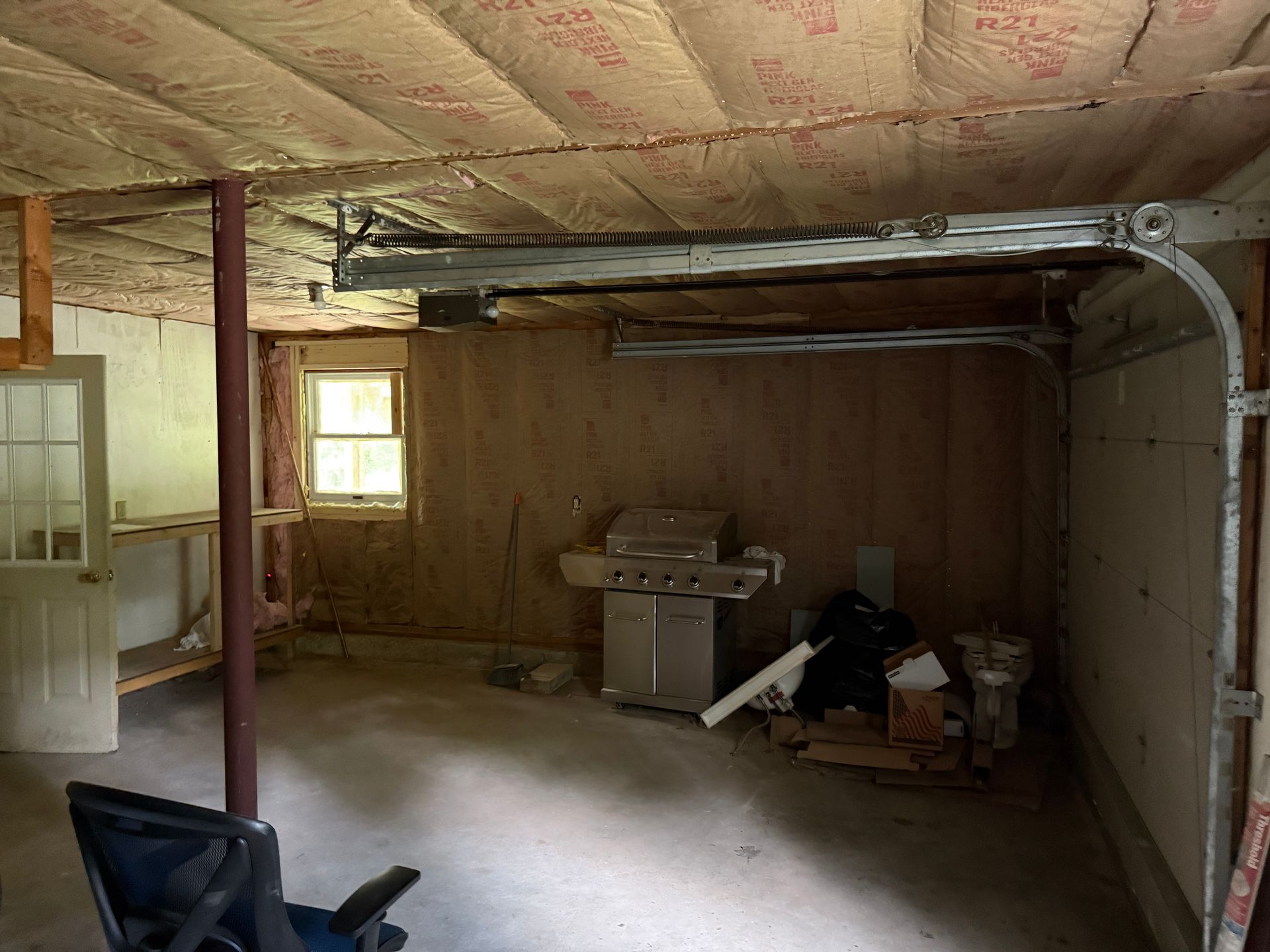 Empty garage interior with garage door opener, insulation, and grill.