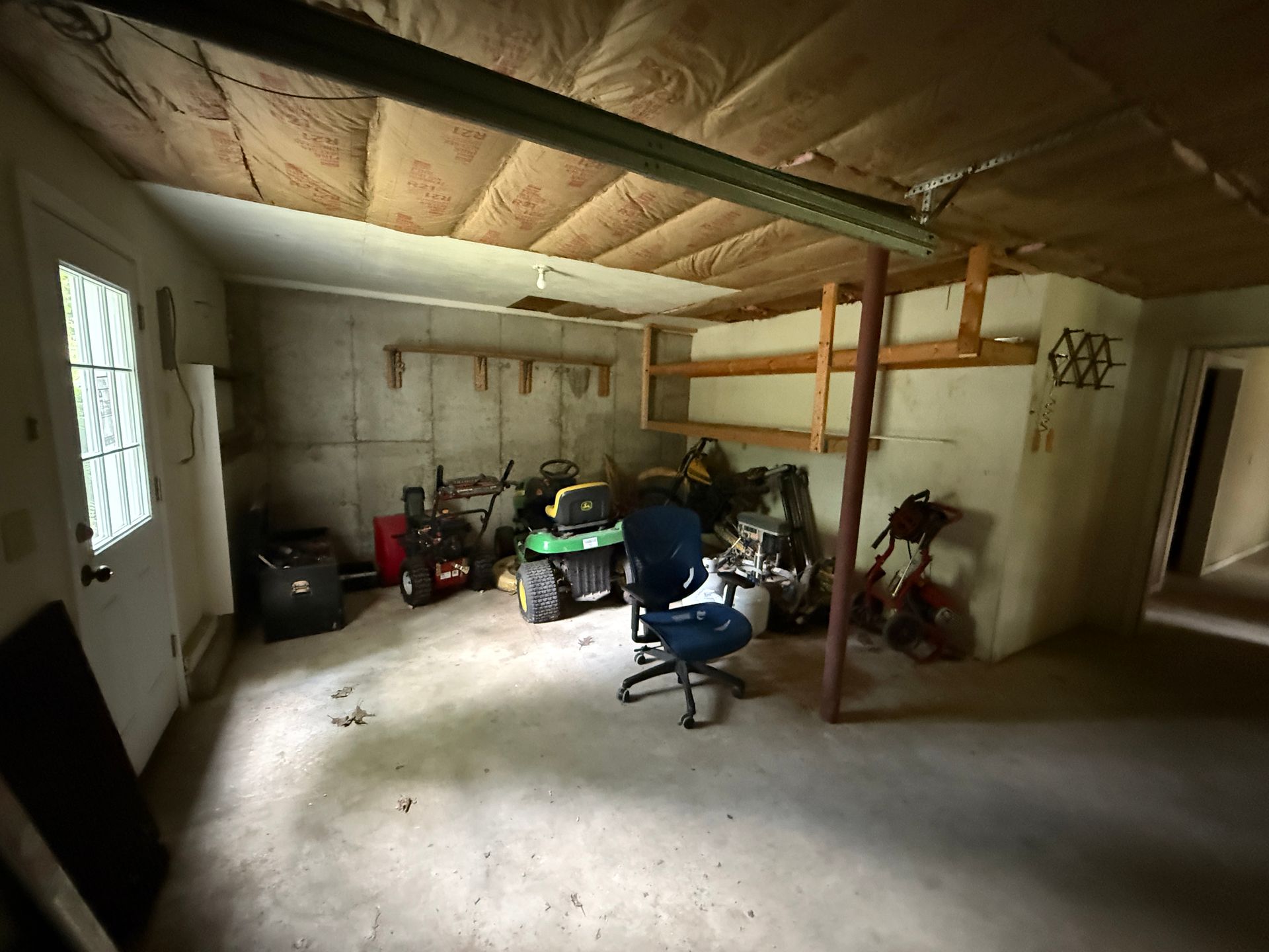 Interior of a garage/storage area with a variety of tools, including a lawnmower, and an office chair.