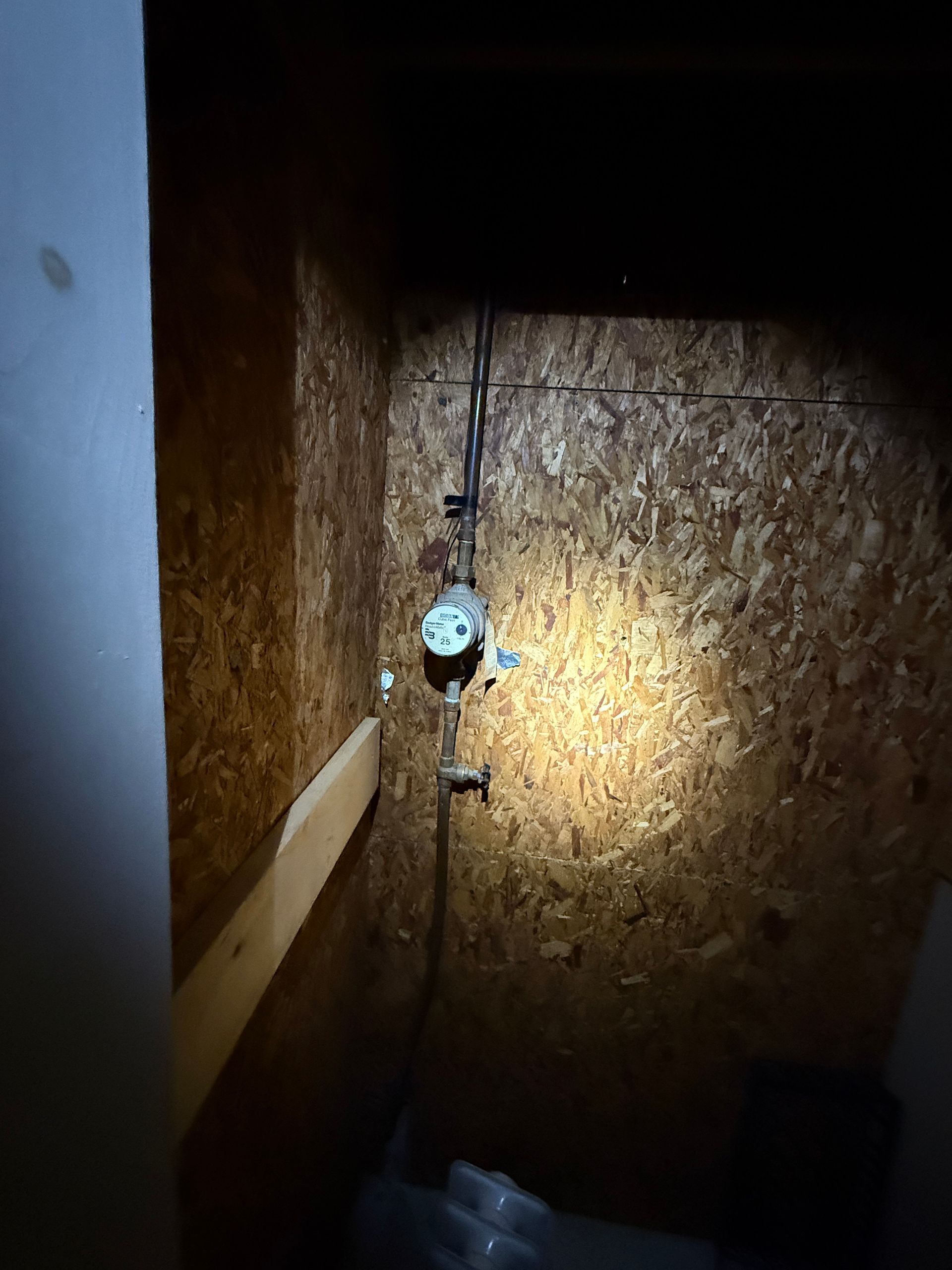 Water meter and pipes against a wood-paneled wall.