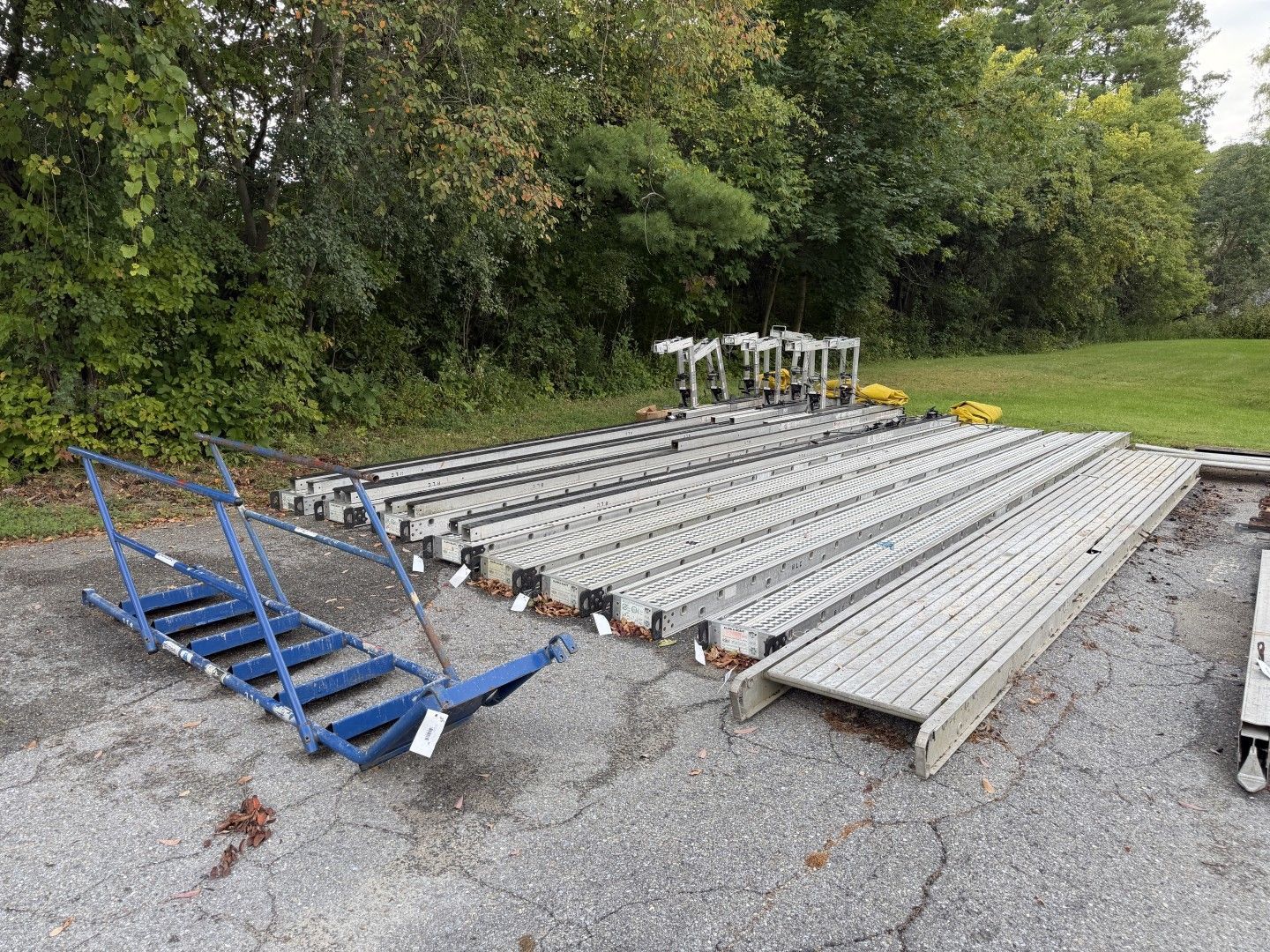 scaffolding stacked on gravel beside a grassy field and trees