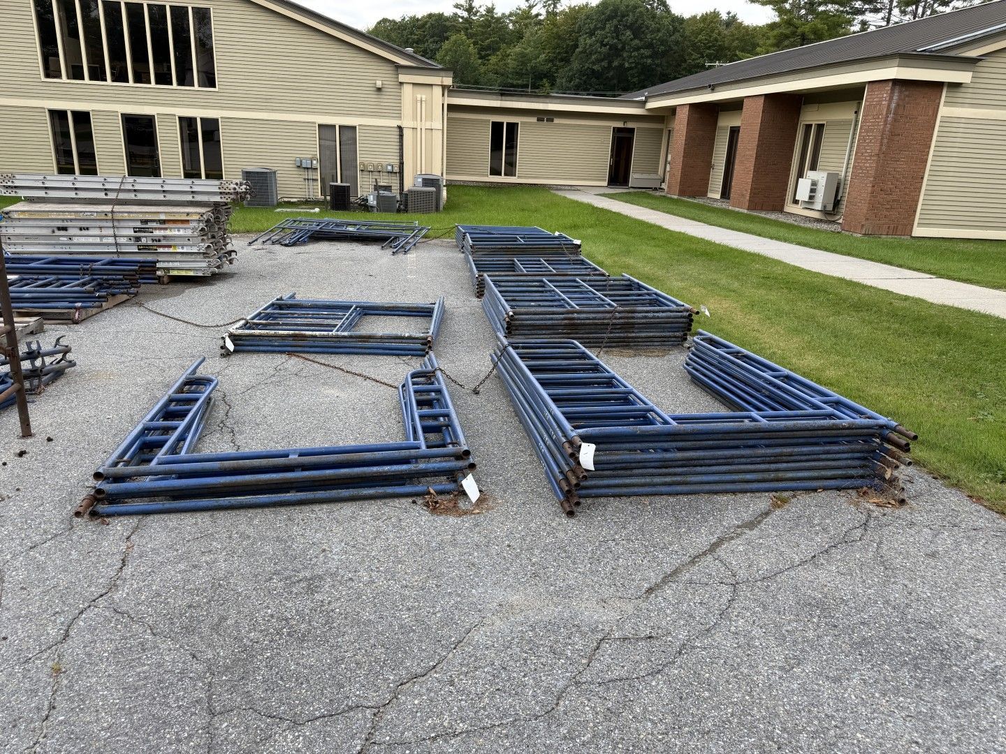 Stacked blue metal frame sections on gravel outside a beige building with a brick walkway.