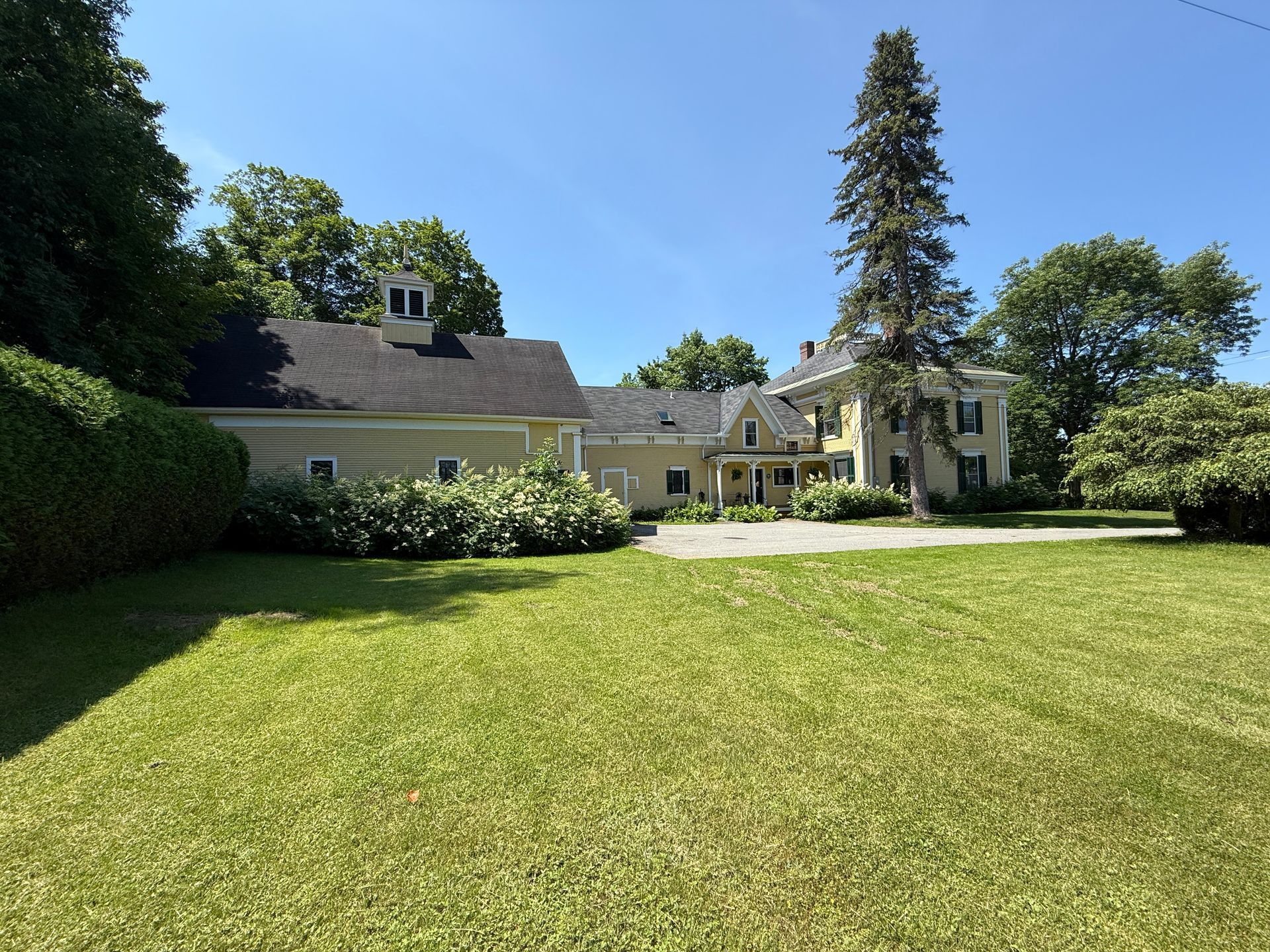 Yellow house with dark roof and green lawn on a sunny day.