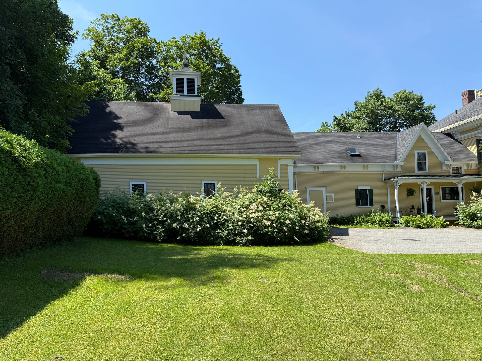 Yellow building with black roof and white trim, surrounded by green lawn and trees under a blue sky.